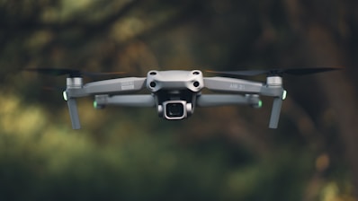A drone is flying in front of green trees.