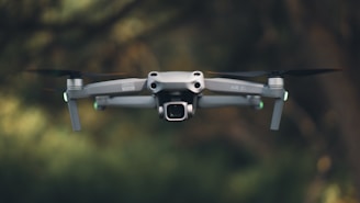 A drone is flying in front of green trees.