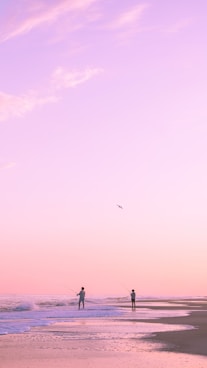 Two people are fishing in the ocean at sunset.