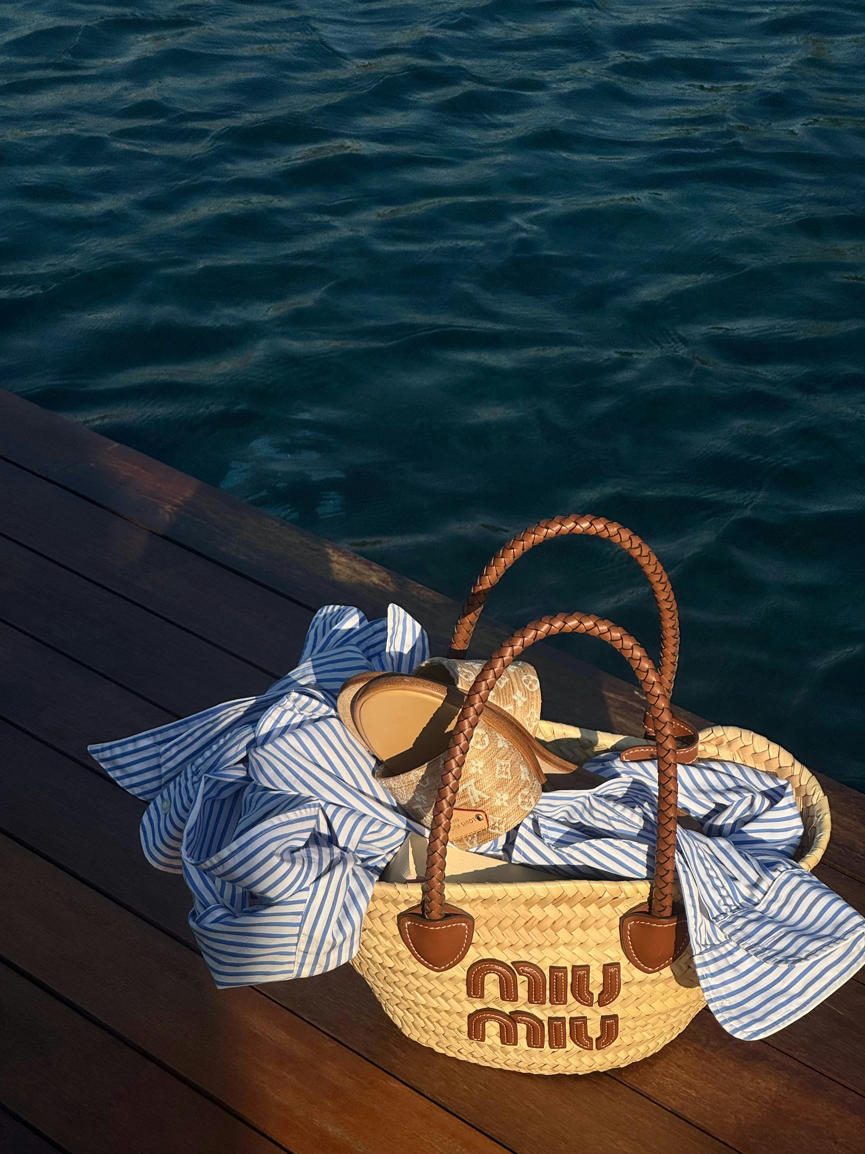 A miu miu bag with beach essentials on a dock.