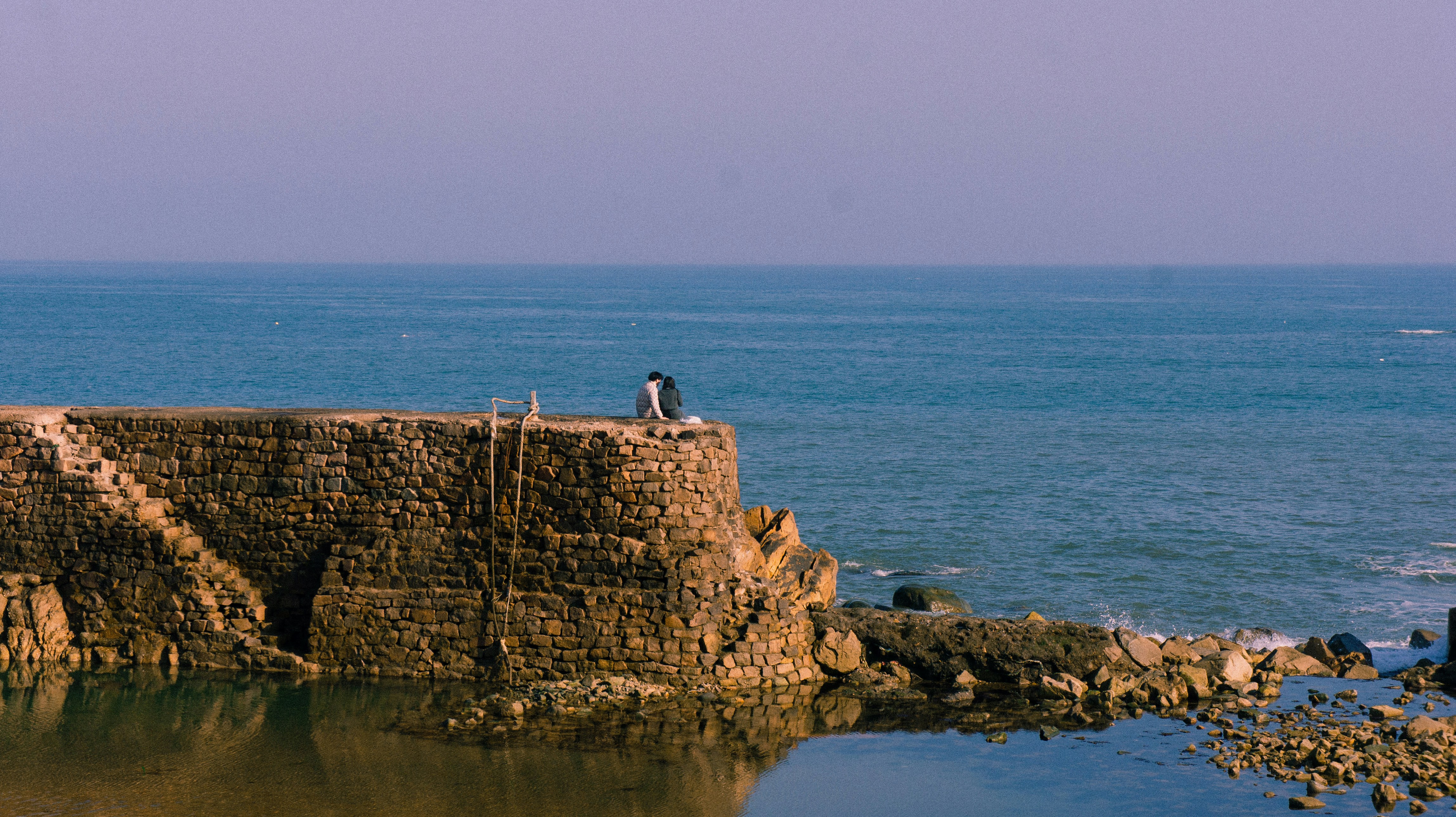 Menschen stehen auf einer Steinmauer in der Nähe des Ozeans.