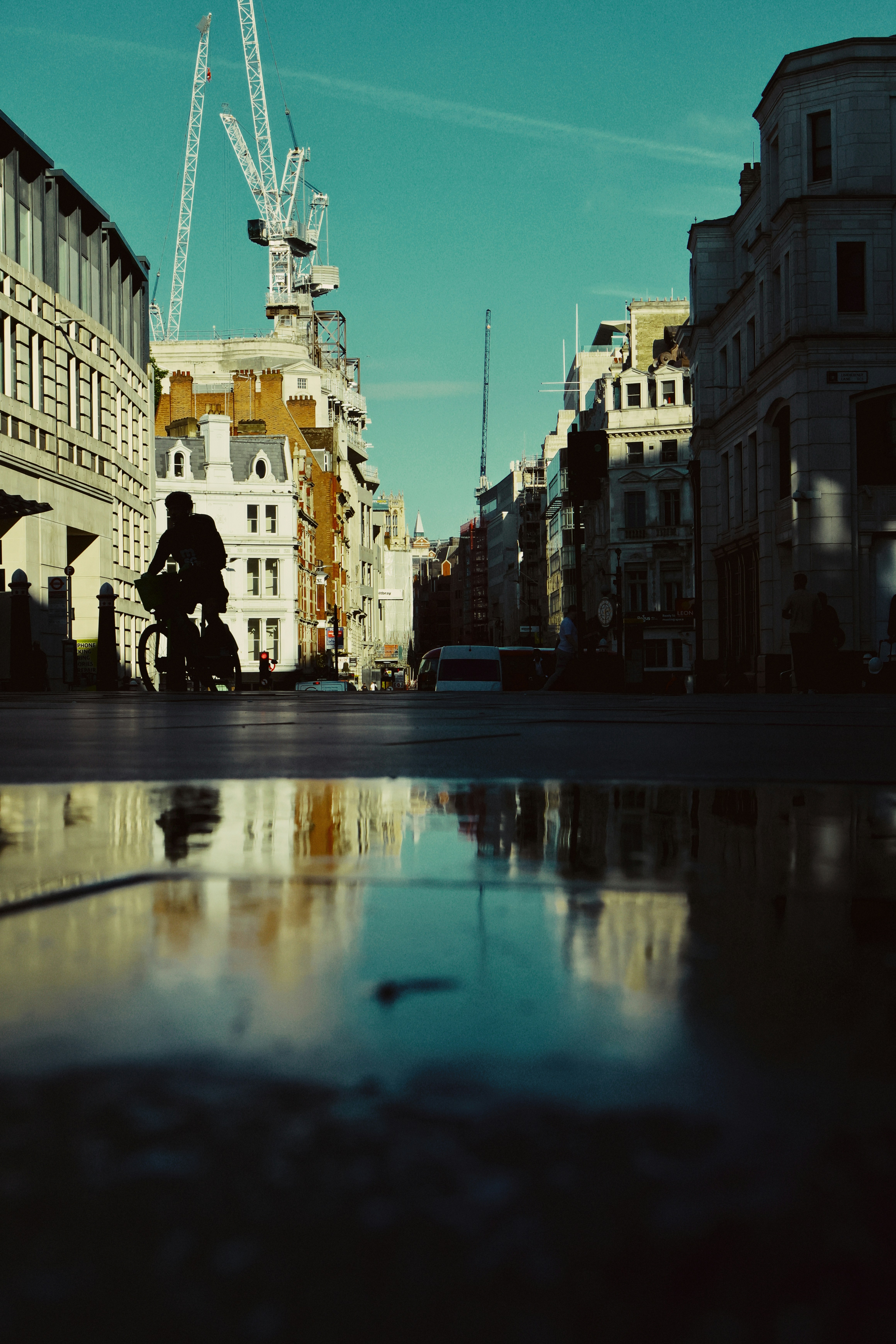 A cyclist rides down a city street with reflections.