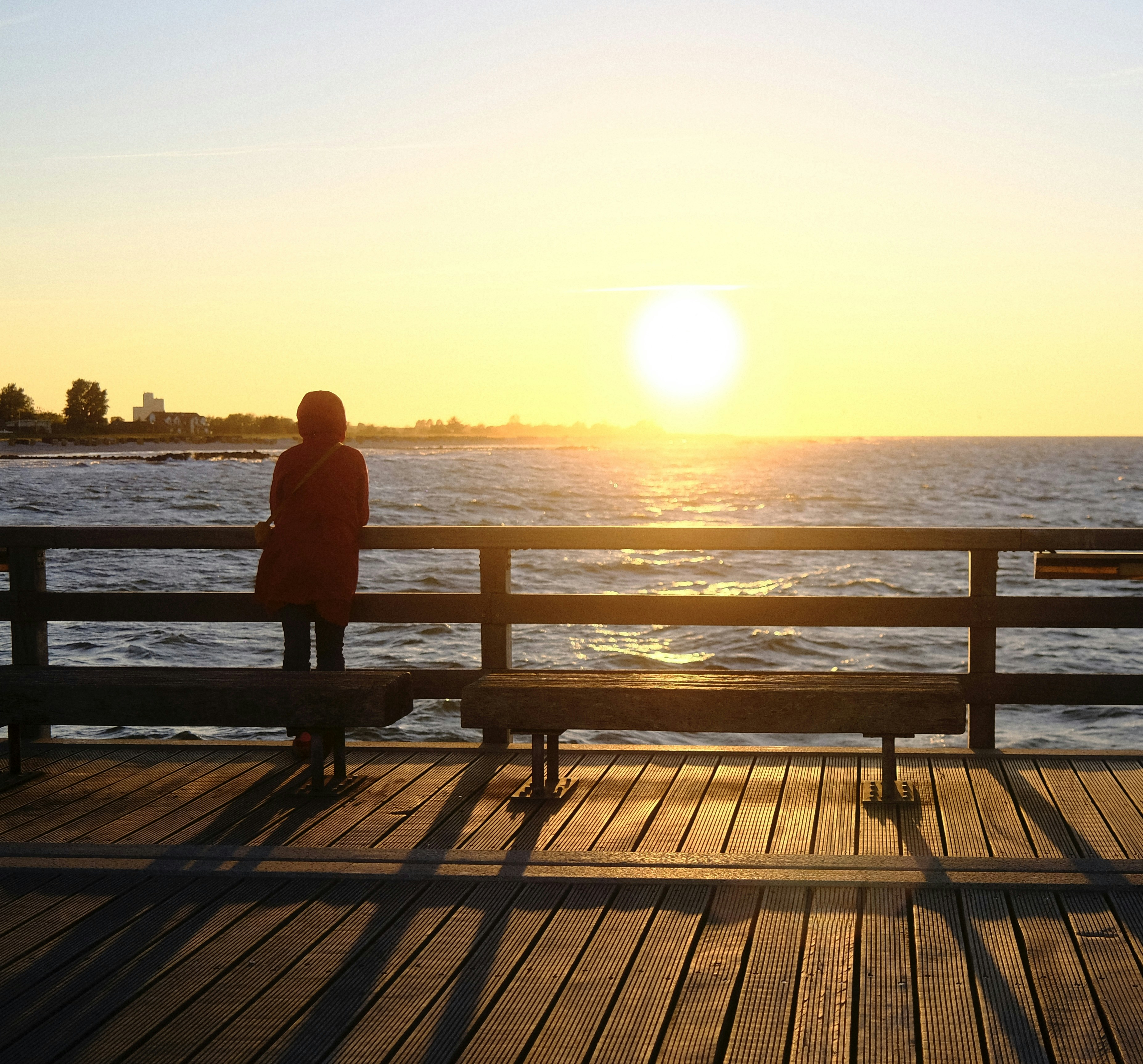Woman watches sunset over the ocean from a pier.