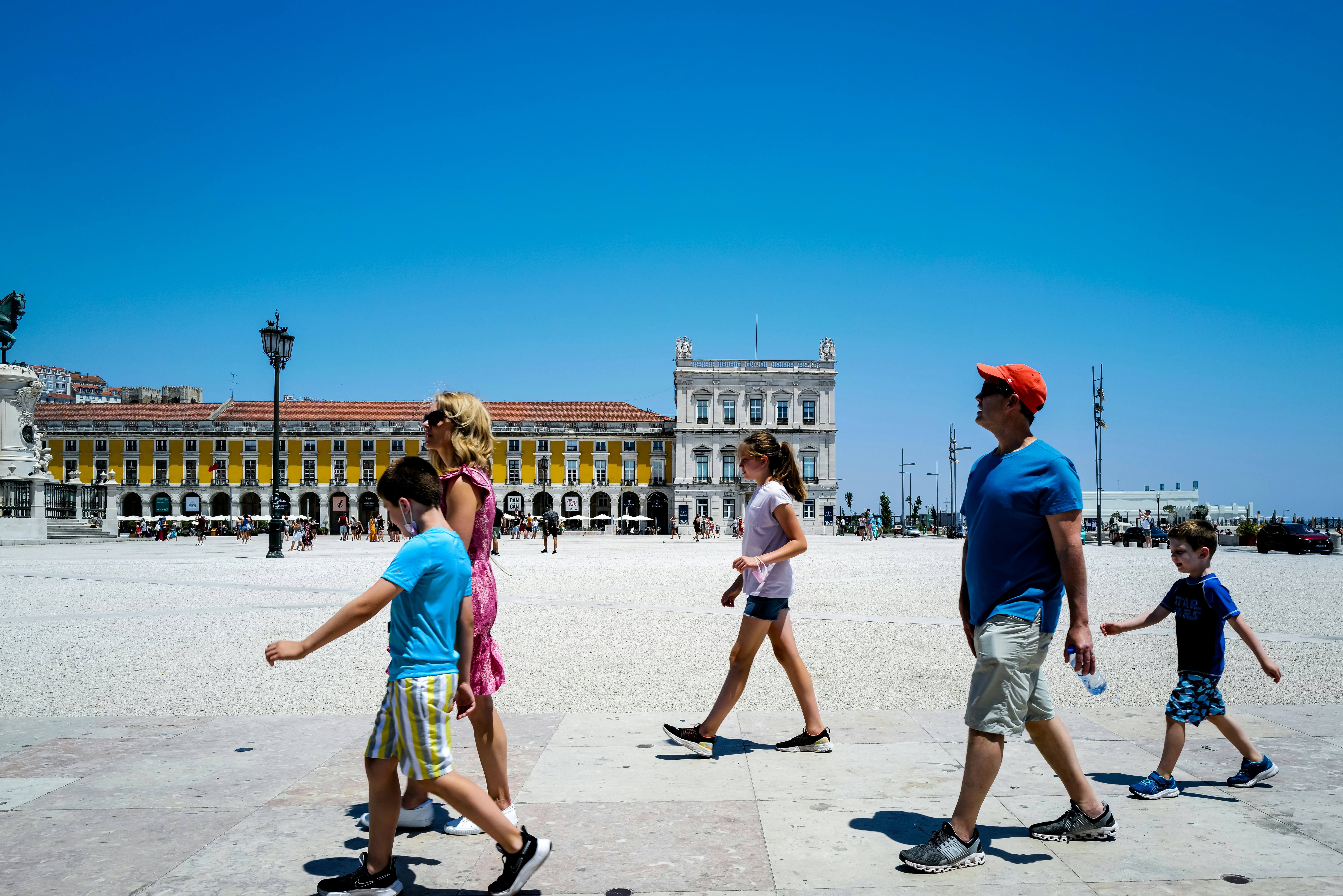A family walks across a sunny, open square.