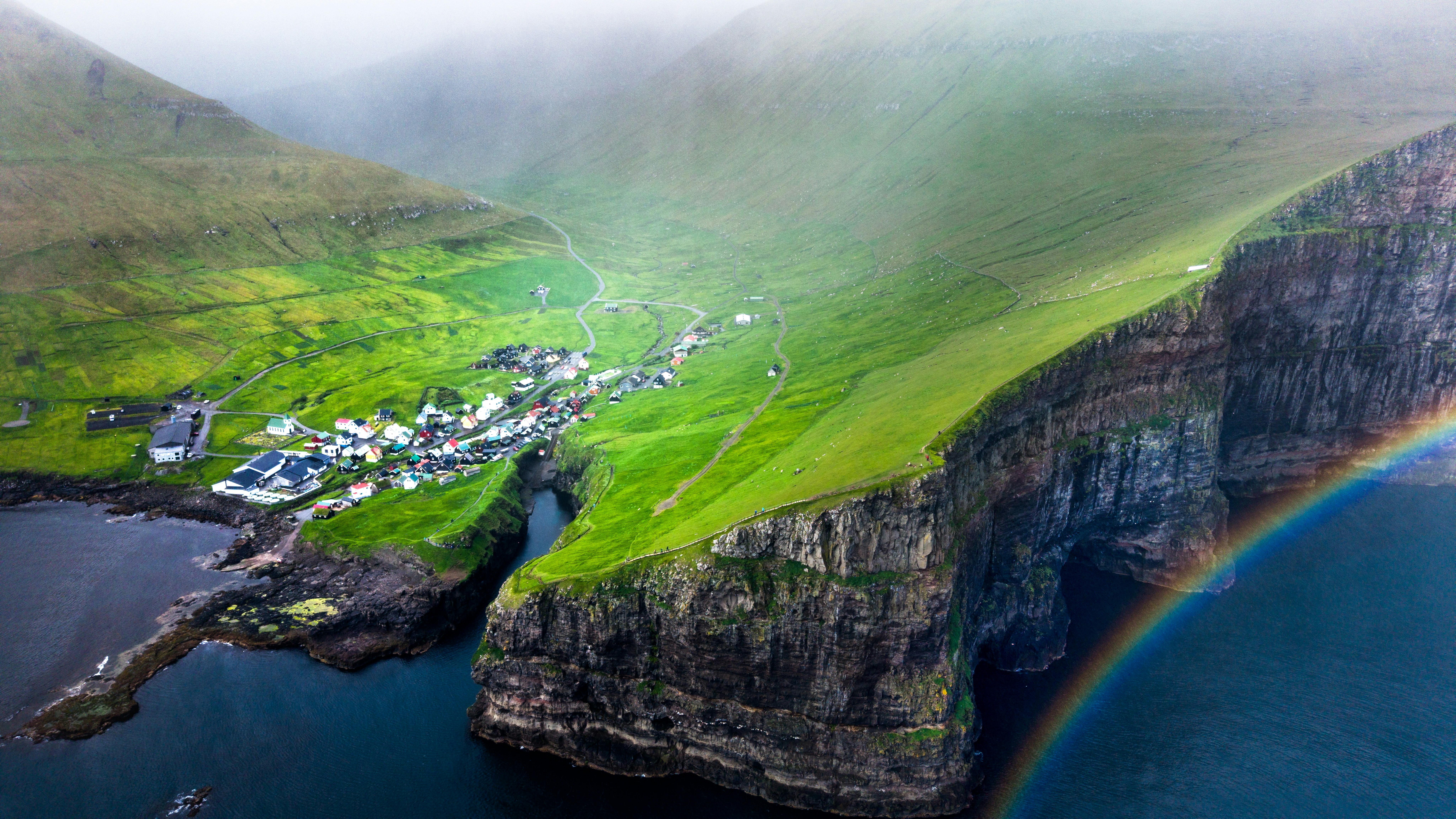 A village is nestled between cliffs and a rainbow.
