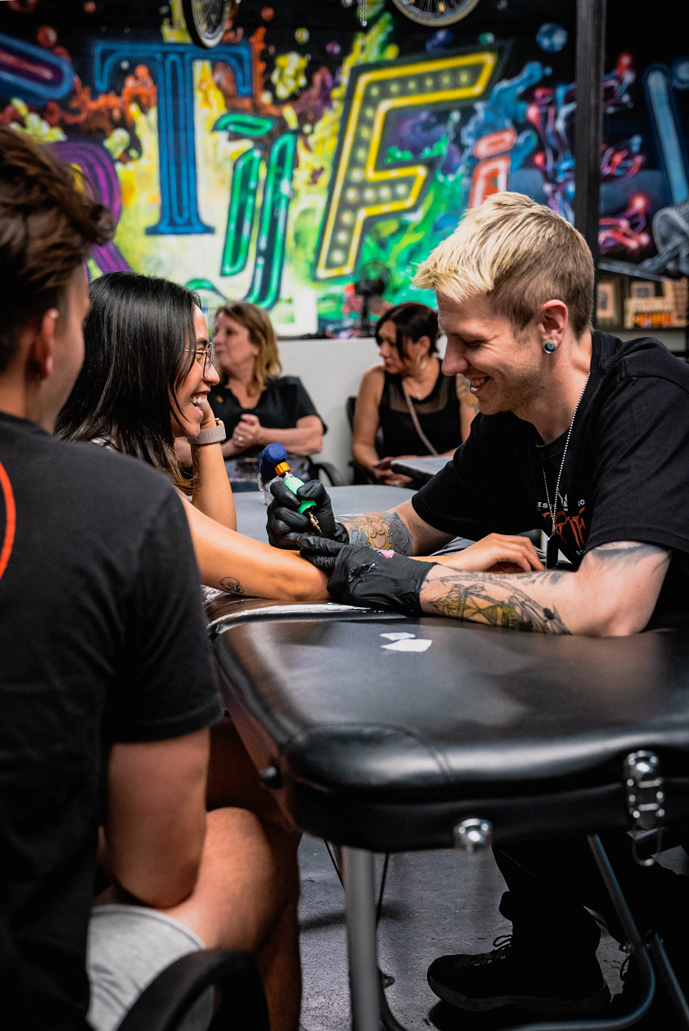 Tatuador sorrindo enquanto tatua o braço de uma cliente