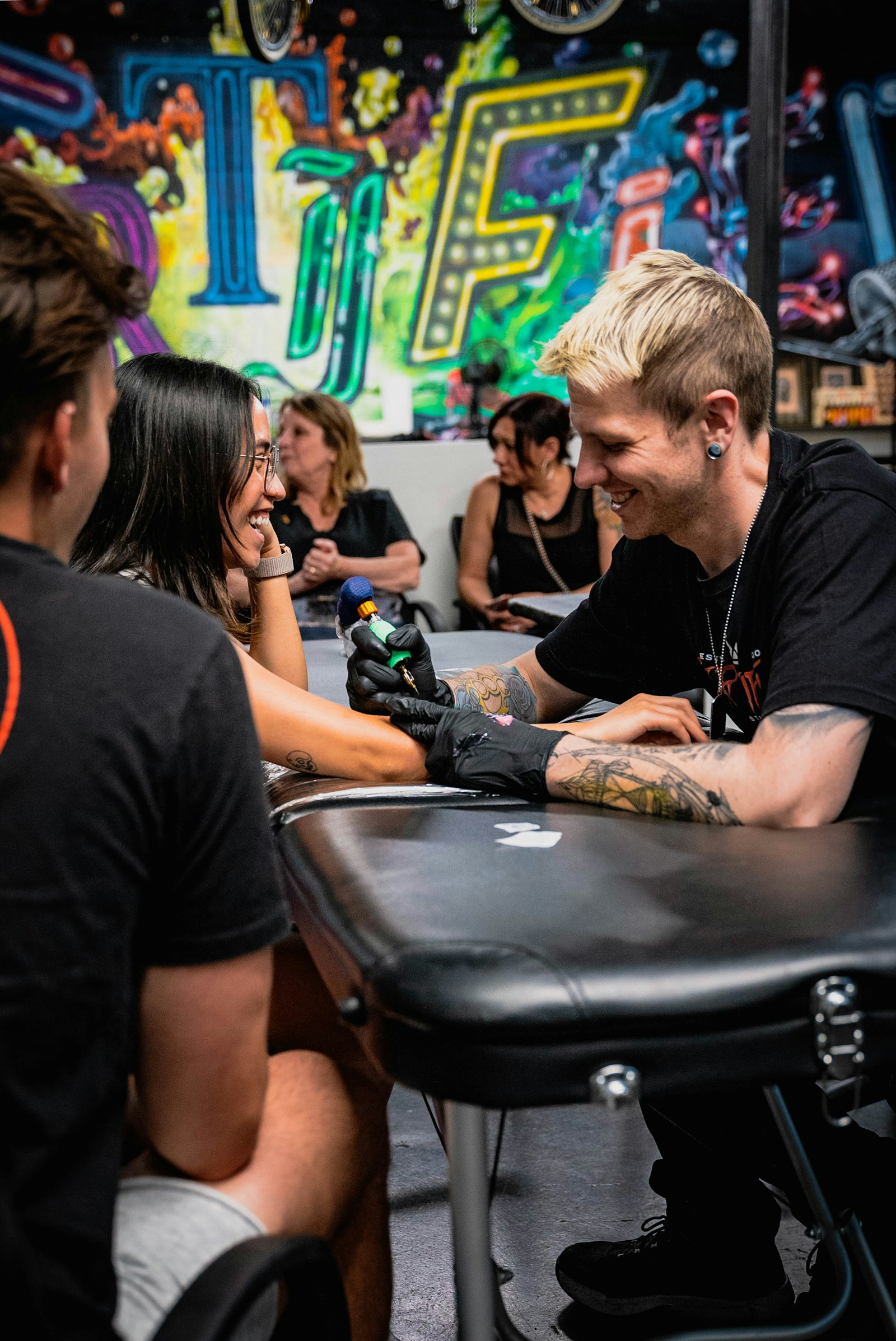 A tattoo artist in nitrile gloves working on a client’s arm in a studio.