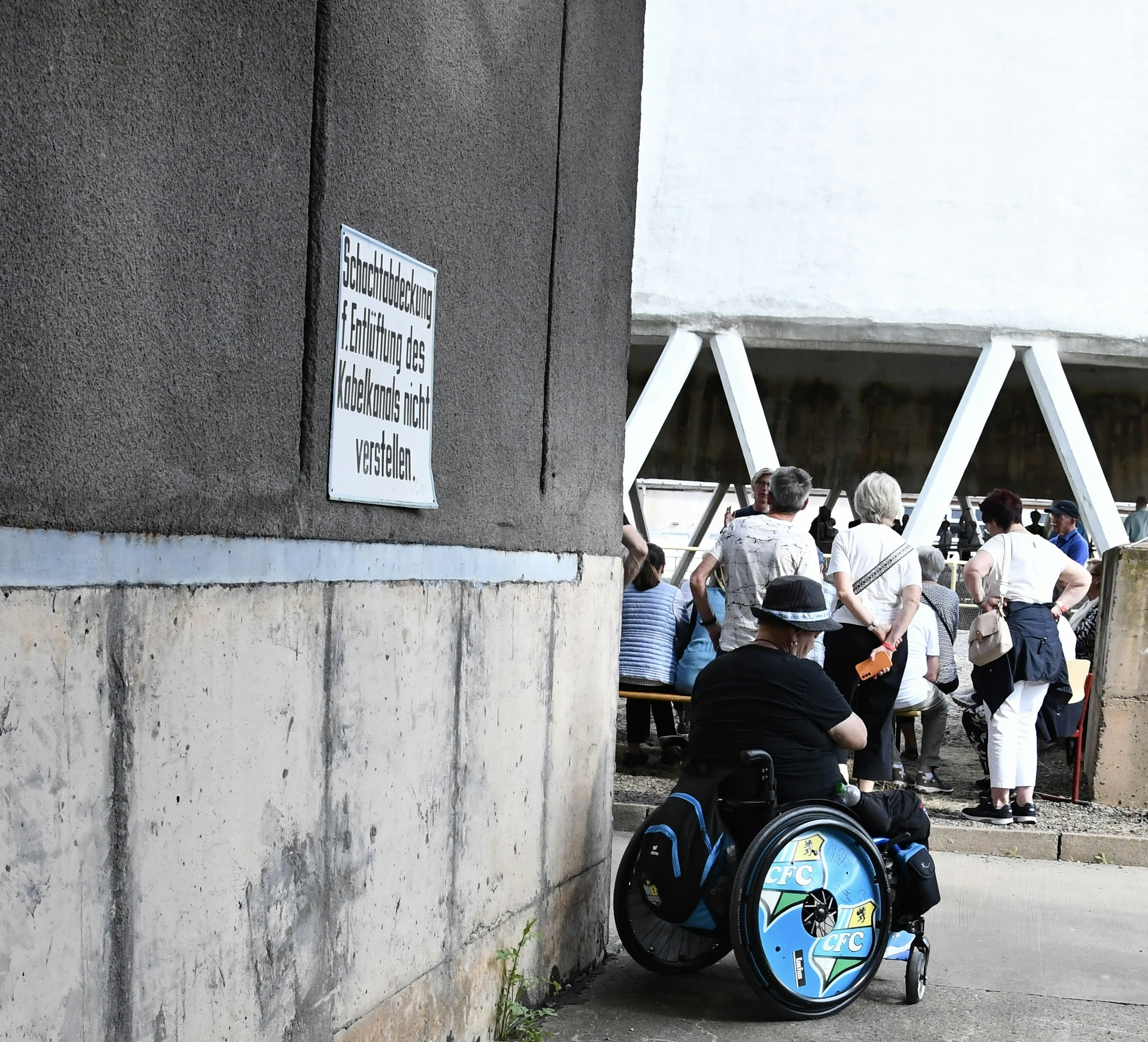 People wait in line, one using a wheelchair.
