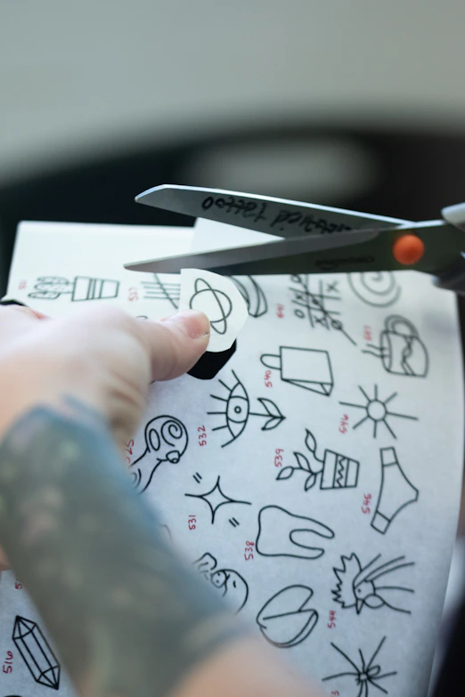 Someone is cutting out a small tattoo stencil