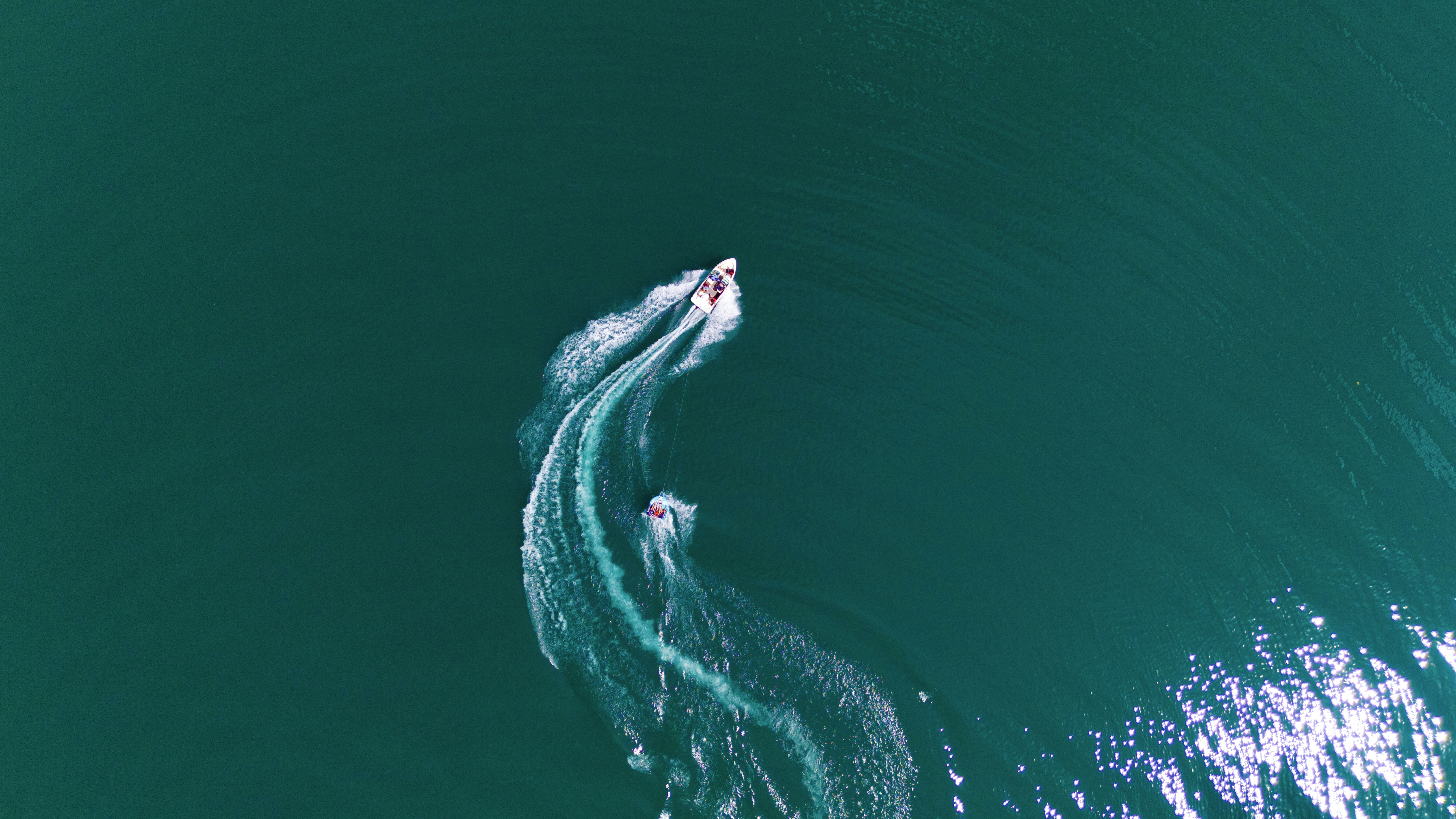 Boats leave trails in the teal ocean.