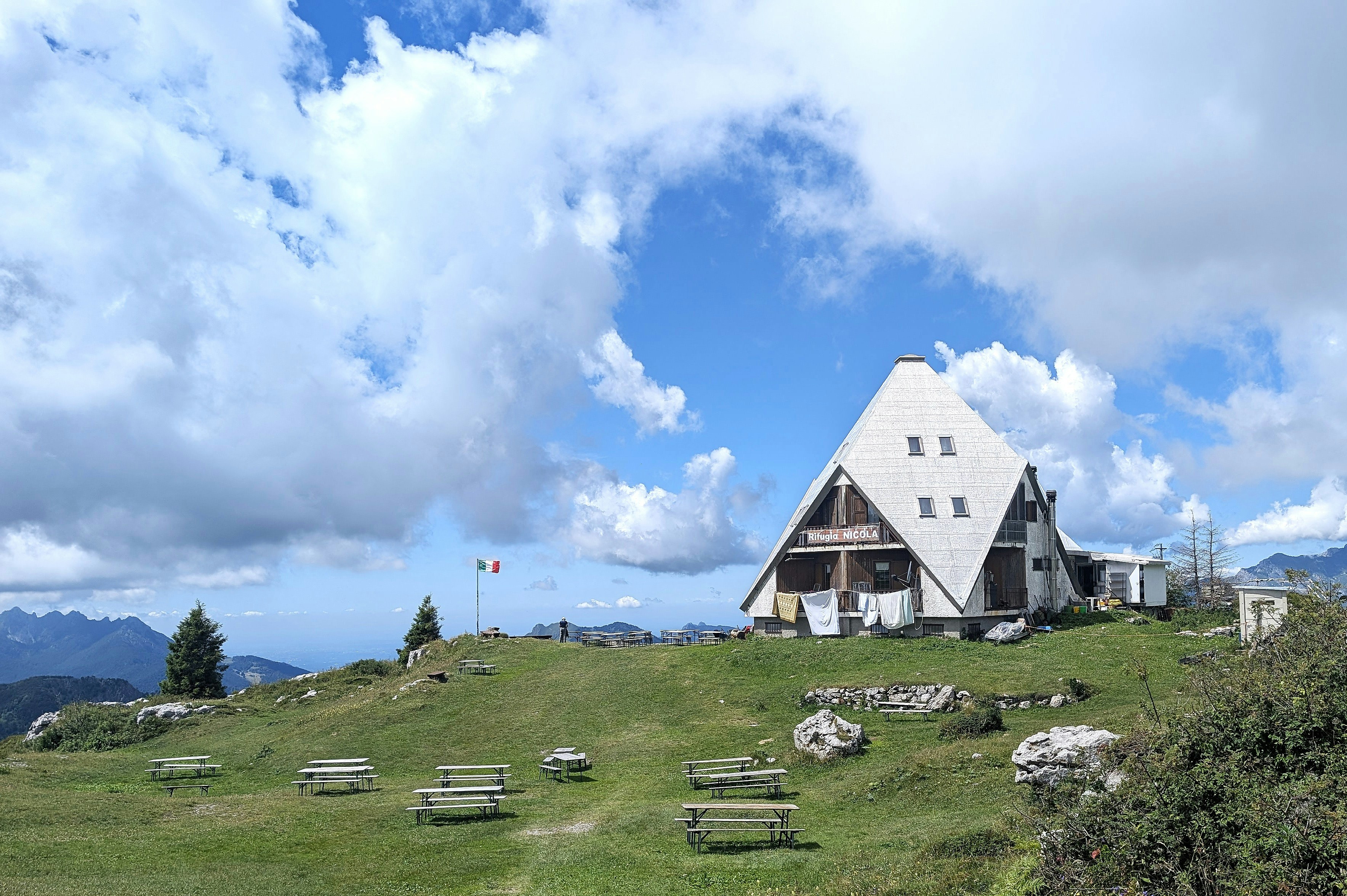 A mountain hut stands atop a grassy hill.