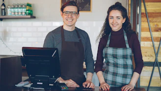 Two smiling cafe workers stand behind a counter.