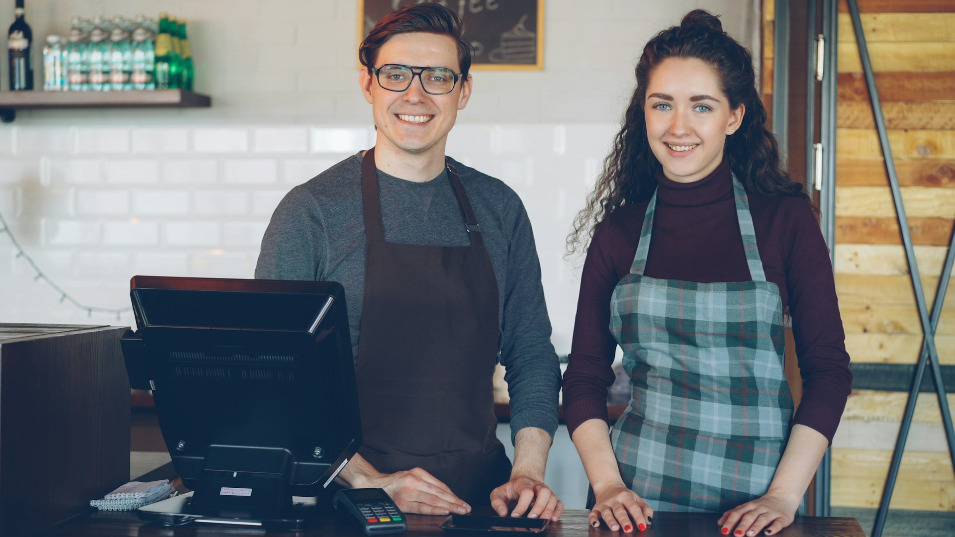 Two smiling cafe workers stand behind a counter.