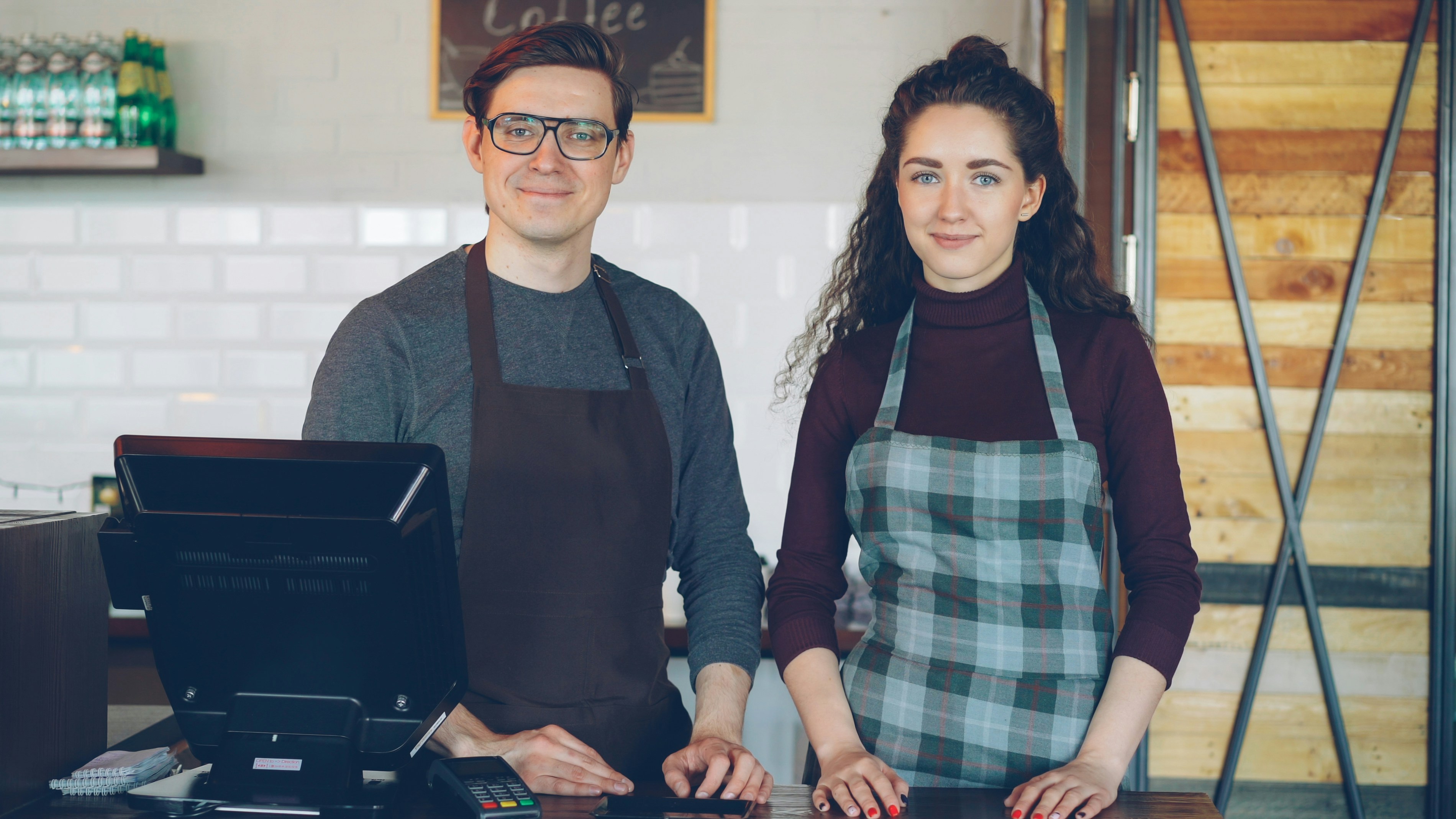 Two baristas are ready for service at their coffee shop.
