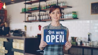 A woman is welcoming customers, as the shop is open.