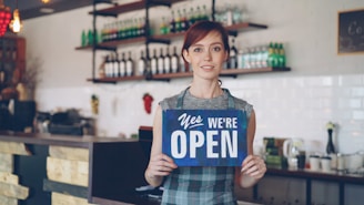 A woman is welcoming customers, as the shop is open.