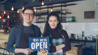 Business owners welcome customers with an "open" sign.