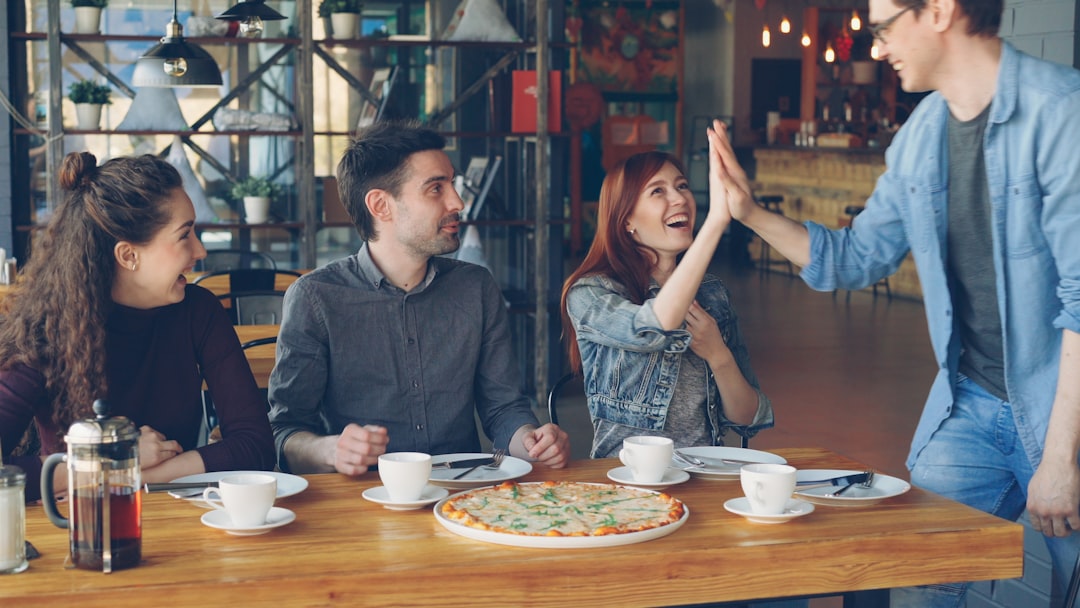 Friends celebrate with a high five over a pizza., Handsome young guy in casual denim clothes is meeting his cheerful fri