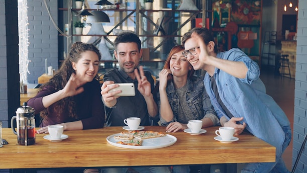 Friends smile and take a selfie at a cafe.