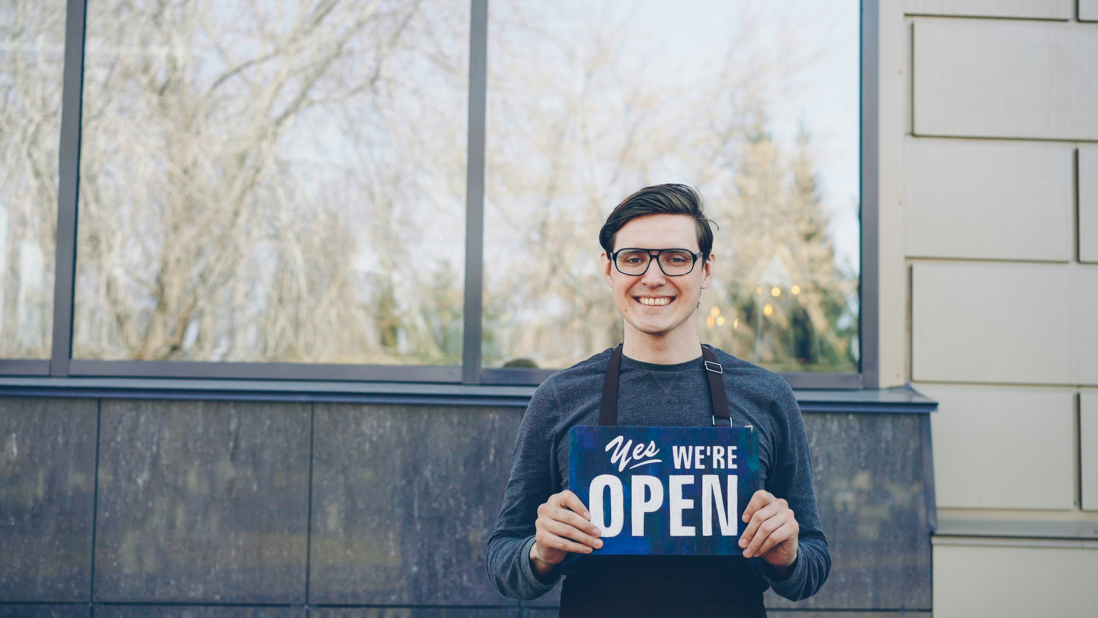 A smiling man holds an "we're open" sign.