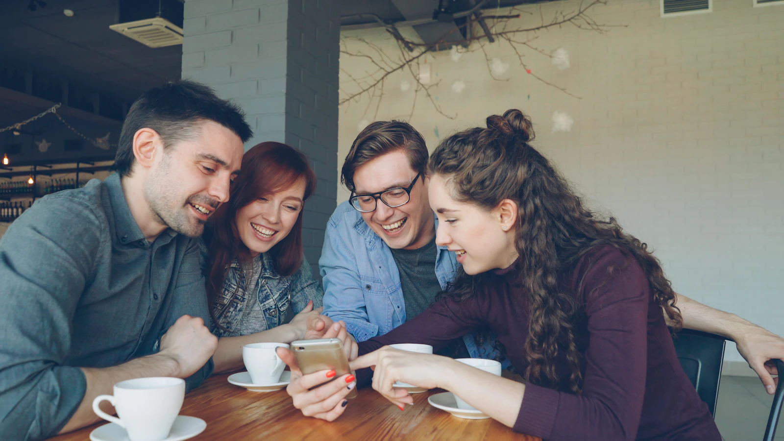 Amigos riendo y mirando un teléfono en un café