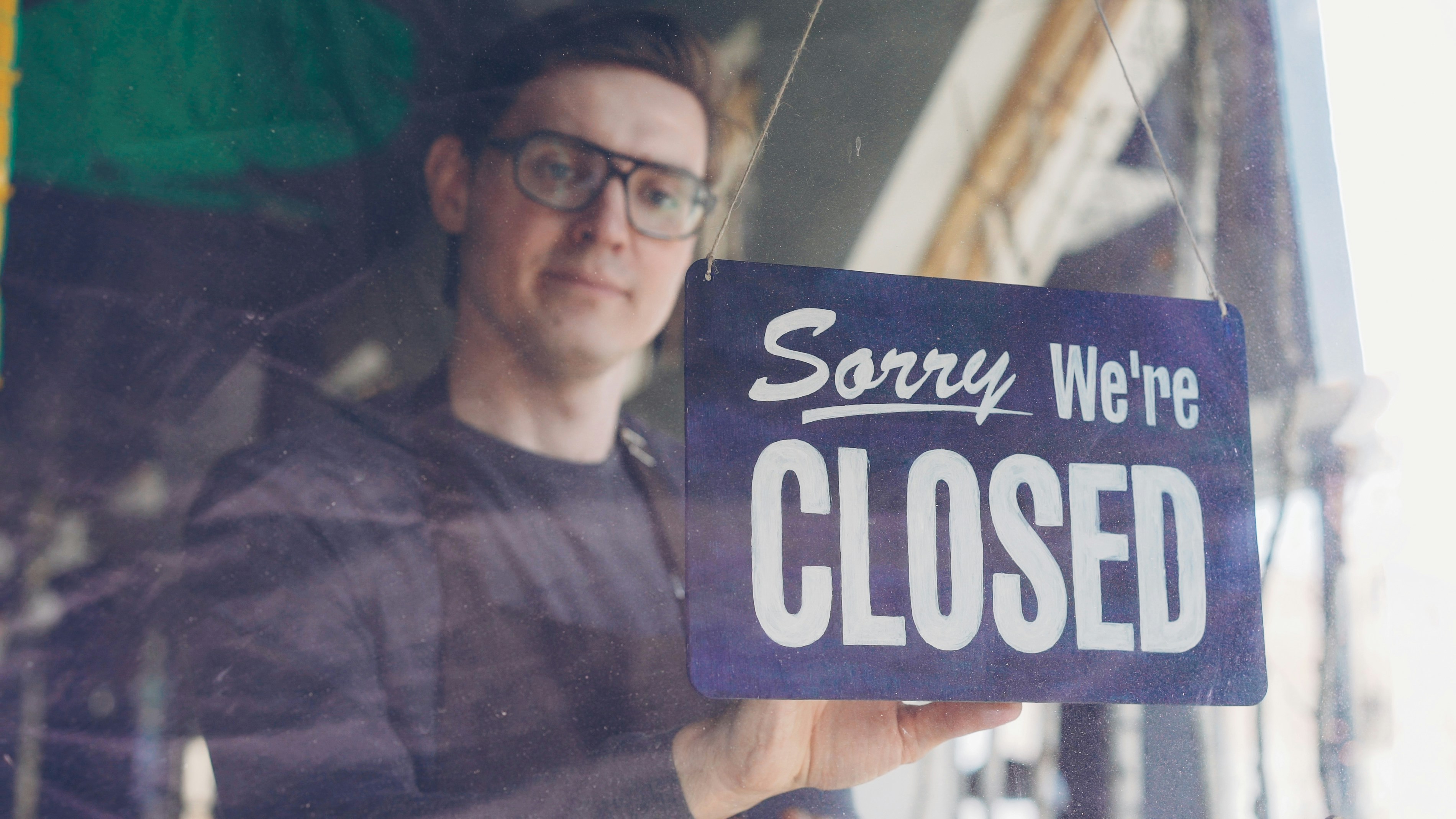Handsome male cafe worker in apron is changing doorplate to sorry we are closed. End of work day, evening and catering business concept.
