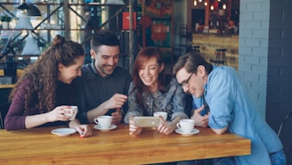 Friends watch a phone in a coffee shop.