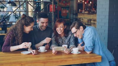 Friends watch a phone in a coffee shop.