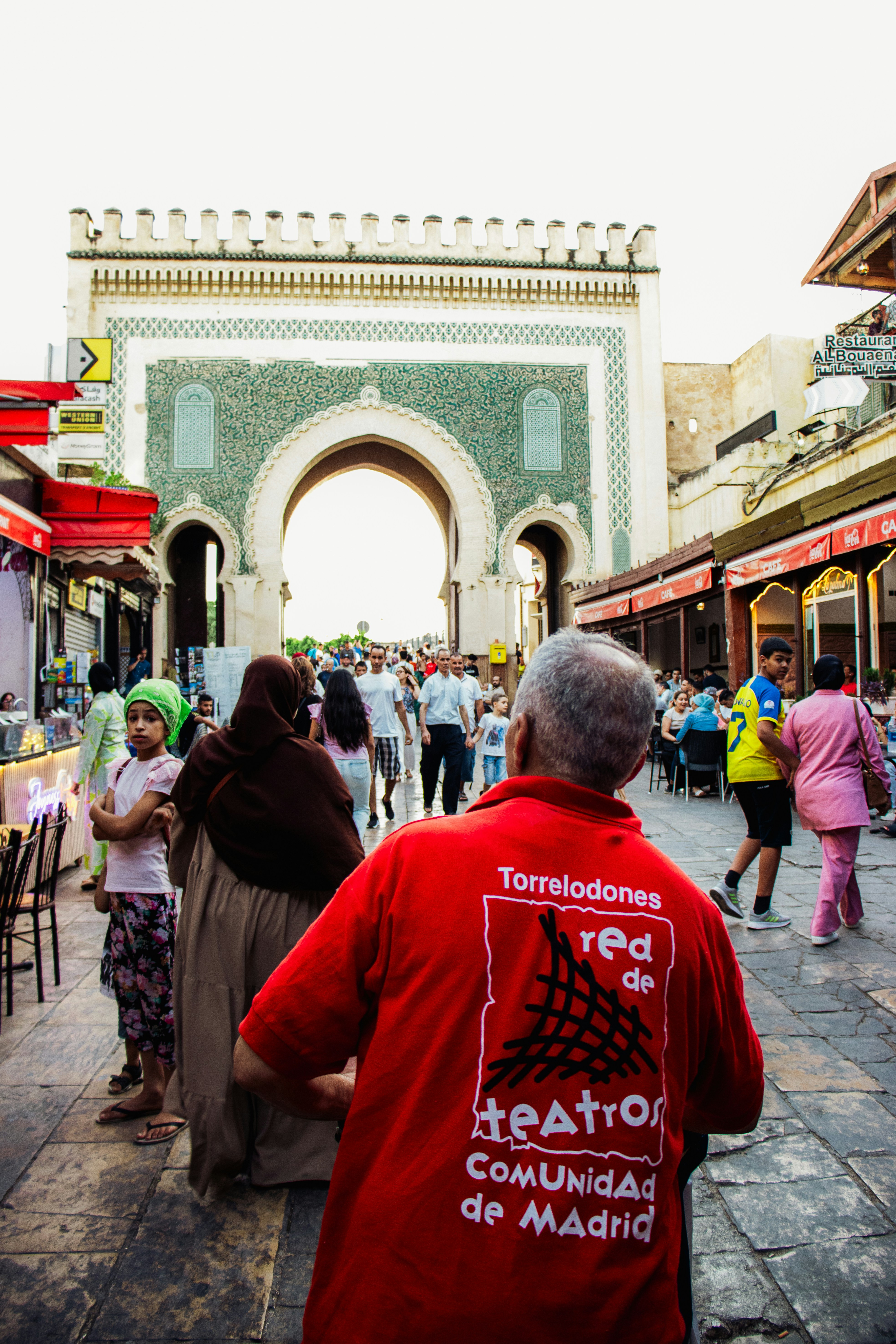 People walk through a market with a large archway.