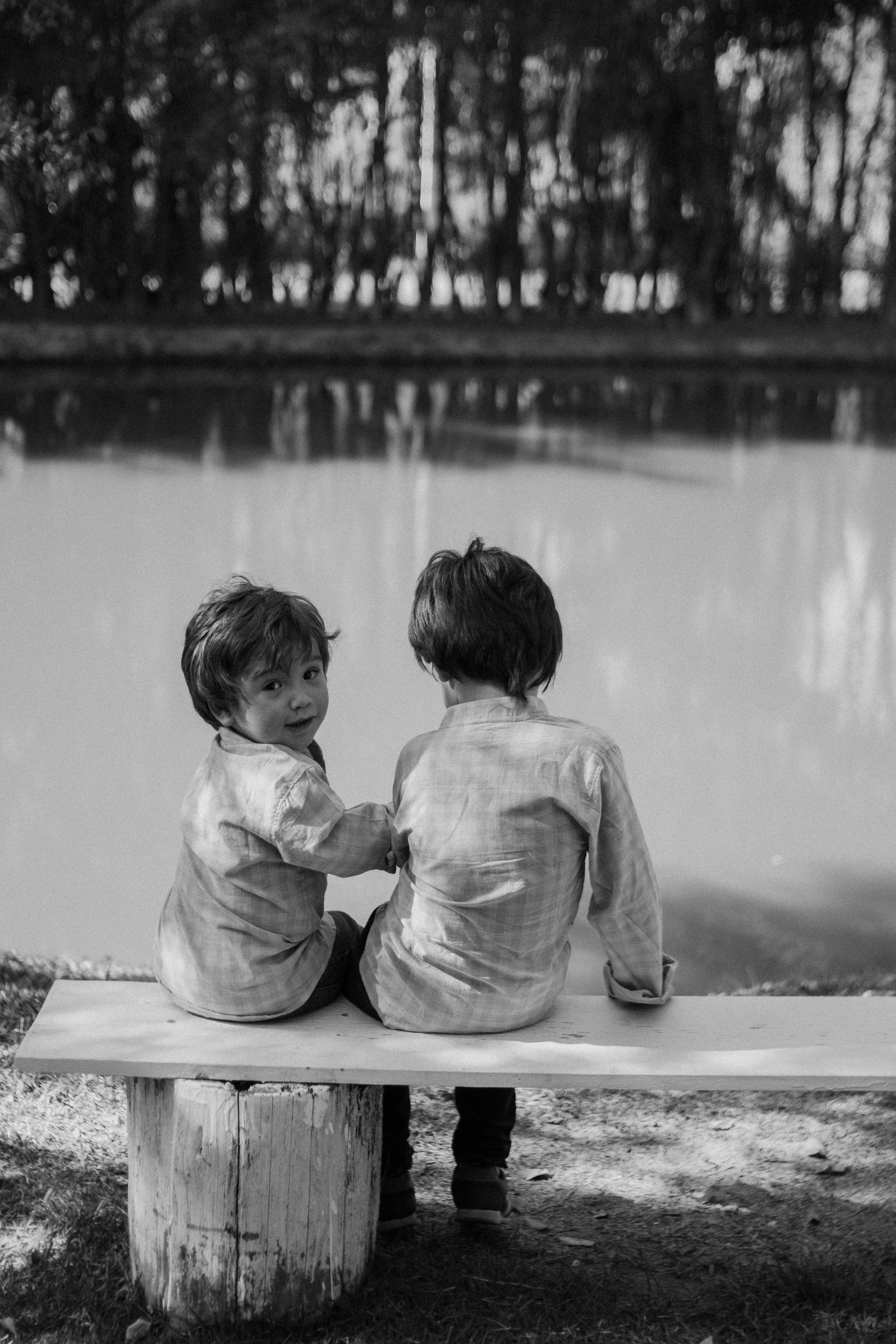 Two kids sit on a bench by the water.
