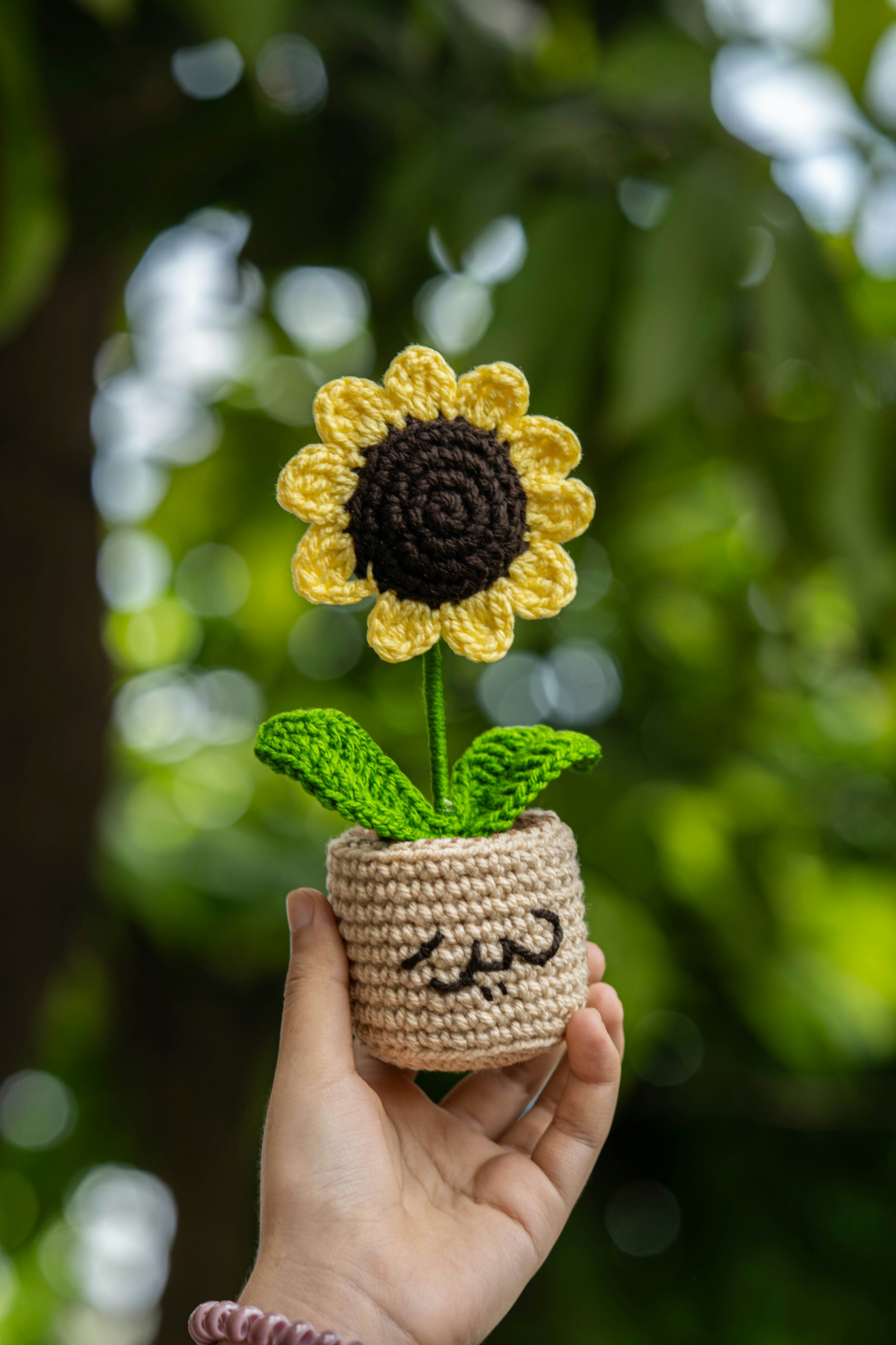A crocheted sunflower is held in someone's hand.