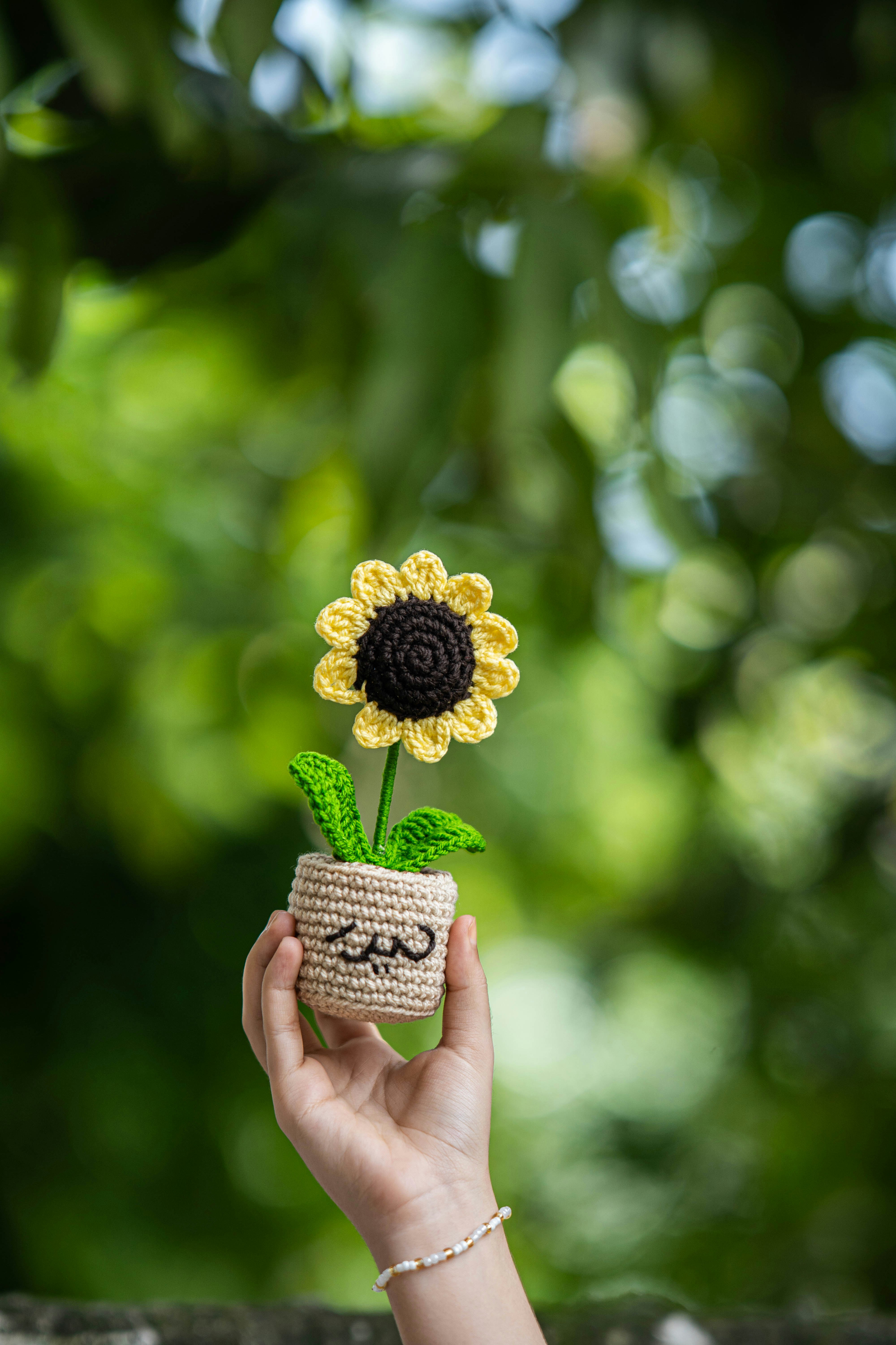 A crocheted sunflower is being held by a hand.