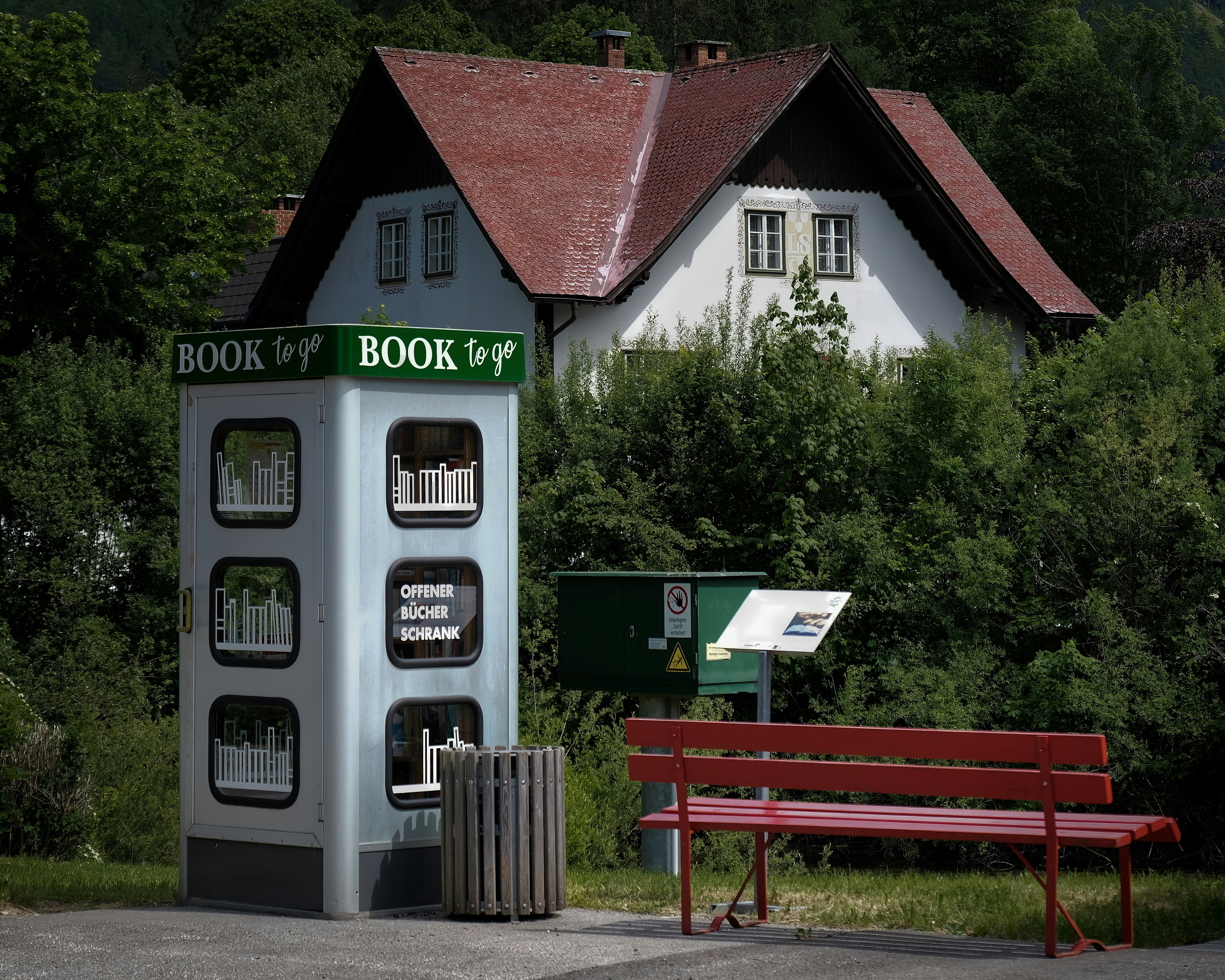 A book to go kiosk sits near a red bench.