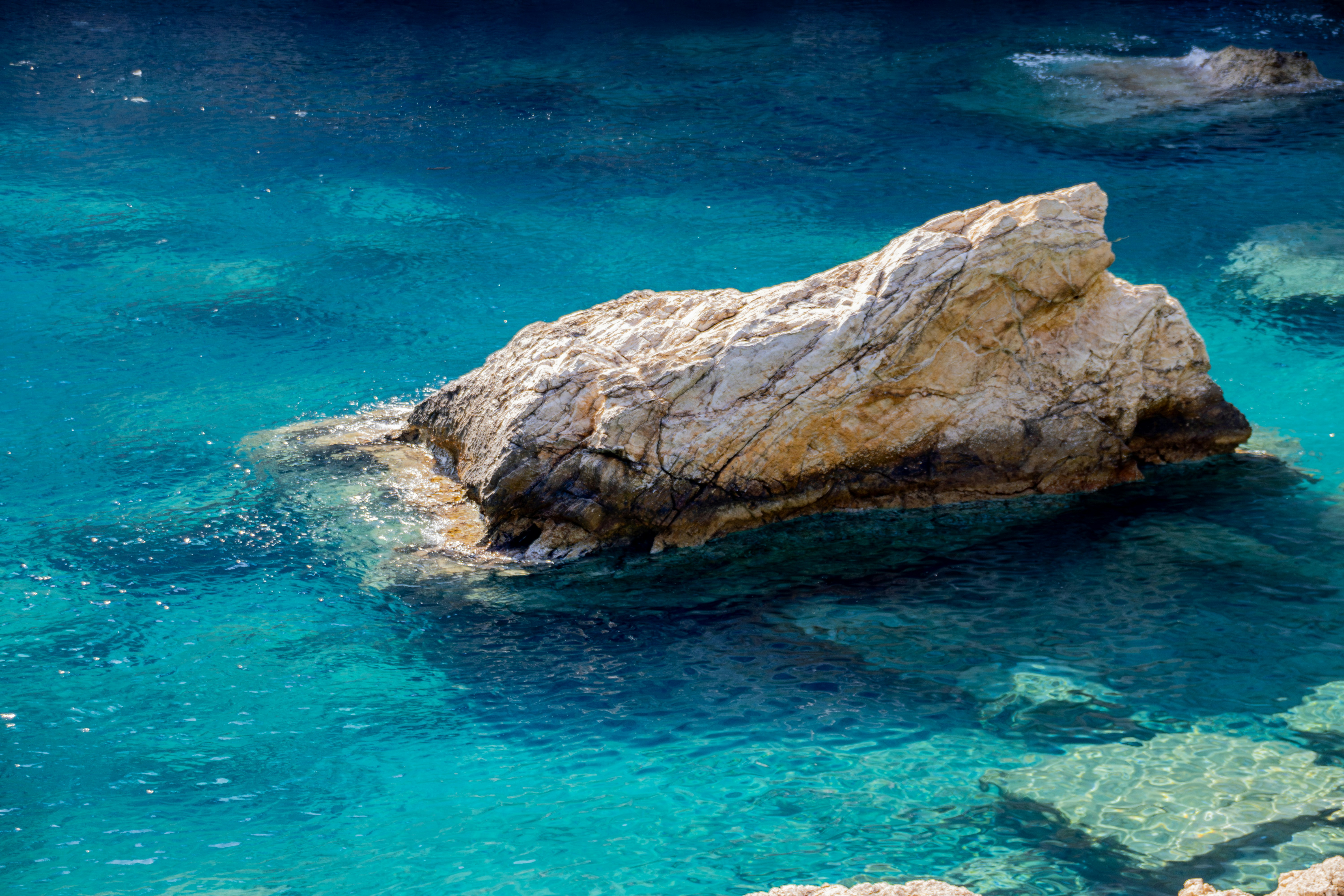 A Large Rock Sits In Clear Blue Water Wallpaper