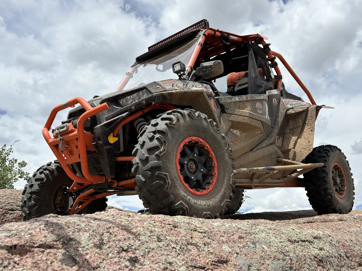 An orange side-by-side with long-travel suspension perched on a rock slab