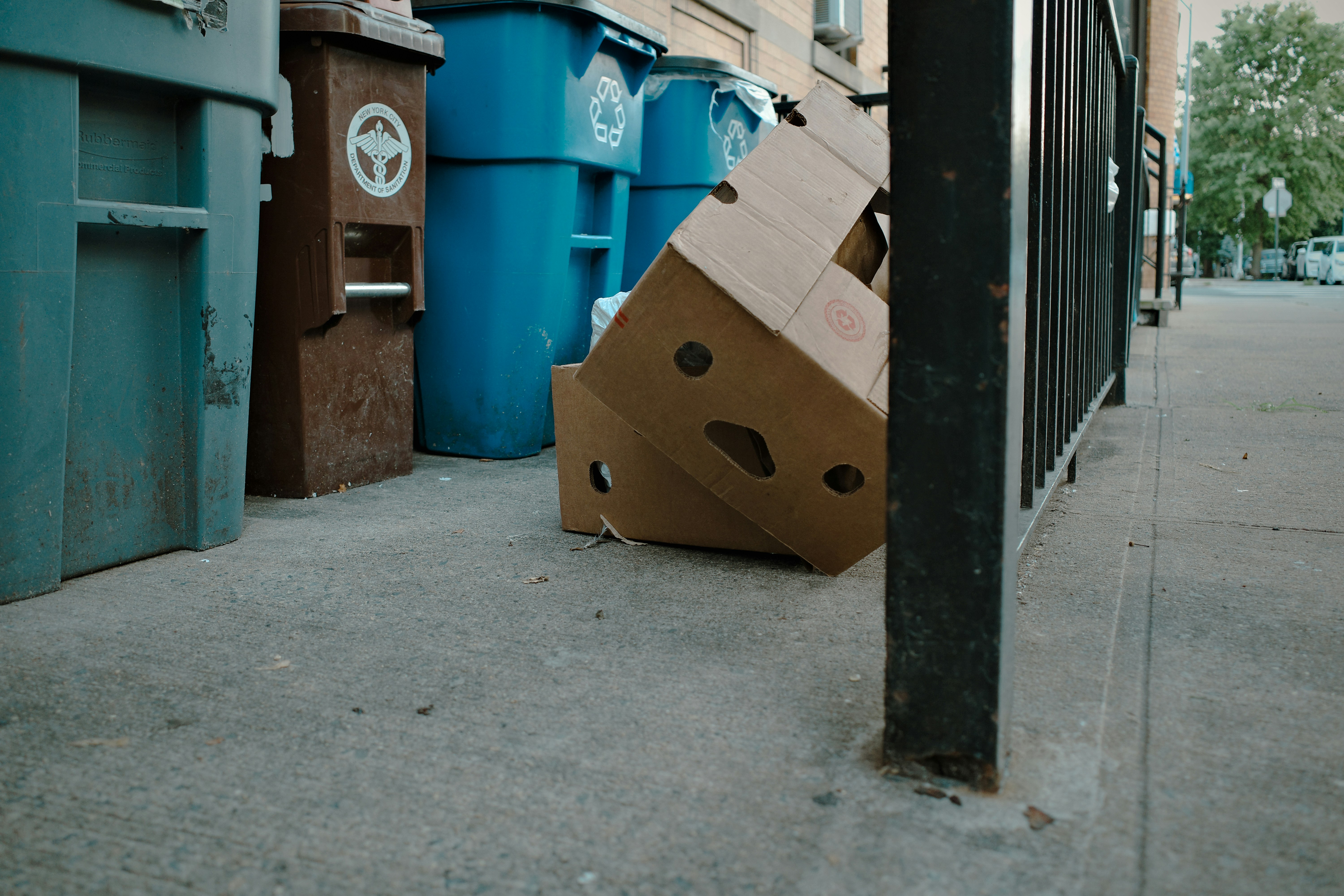 Cardboard boxes are near trash cans on a sidewalk.