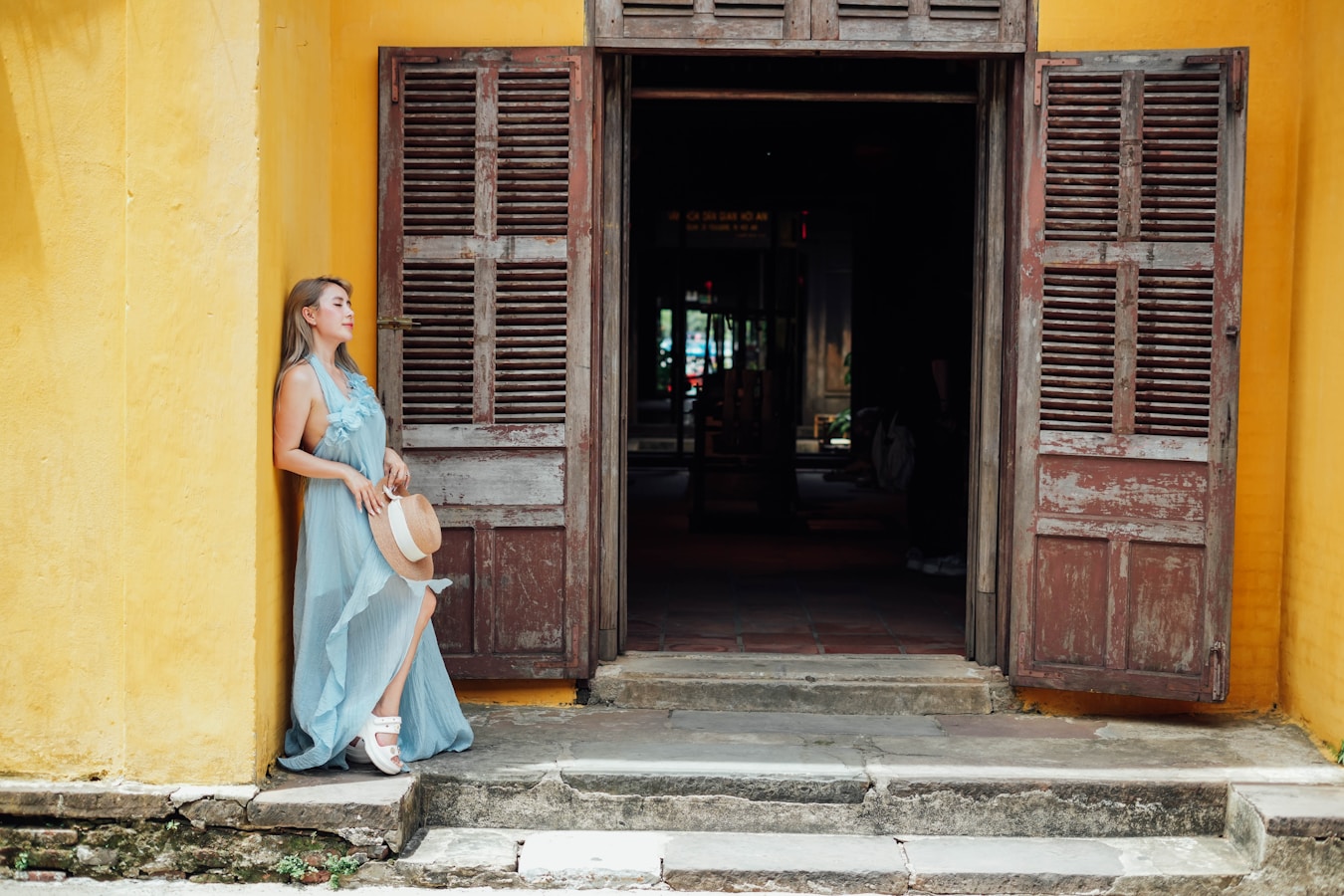 Woman stands in doorway of old, yellow building.
