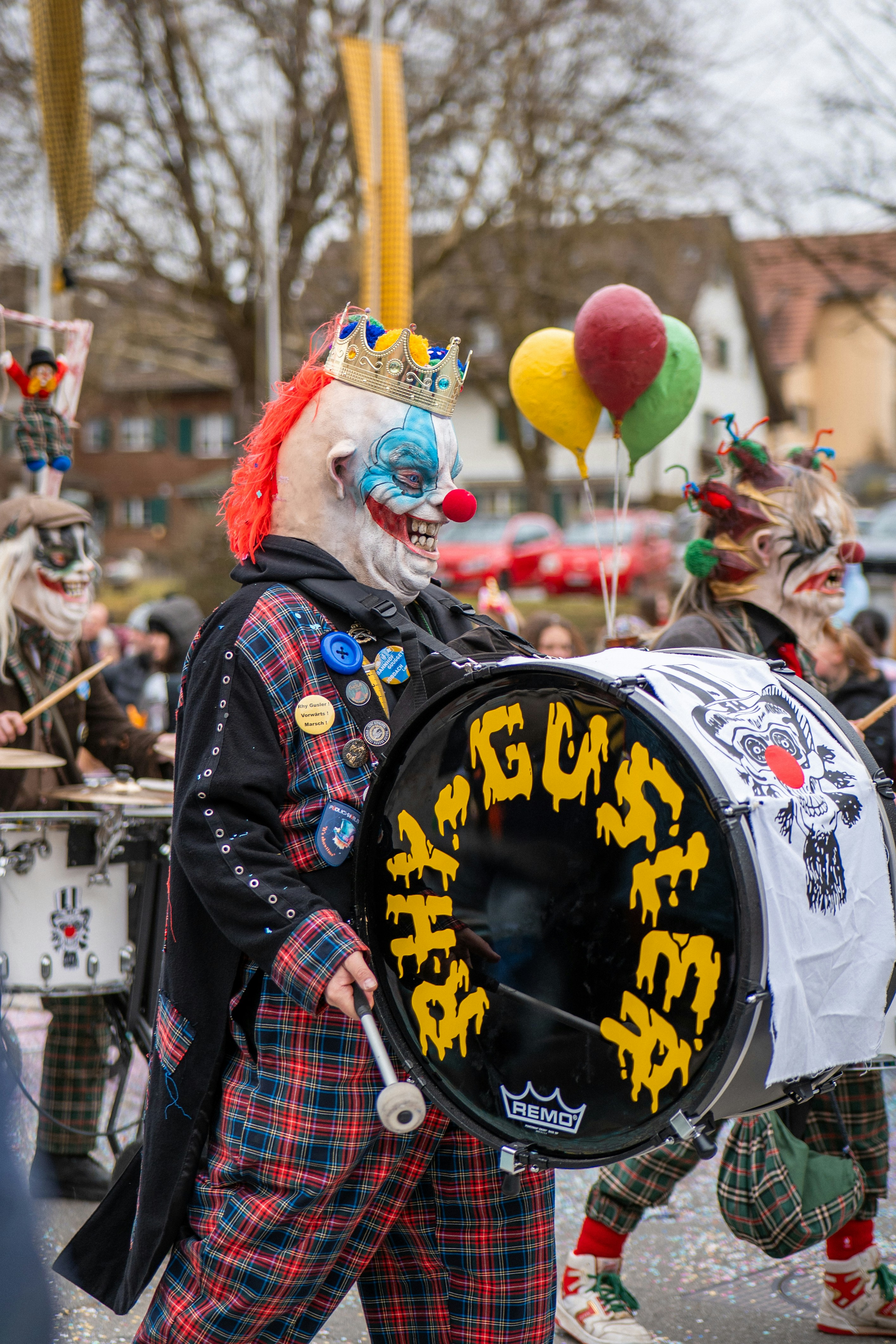 A clown plays a drum at a parade.