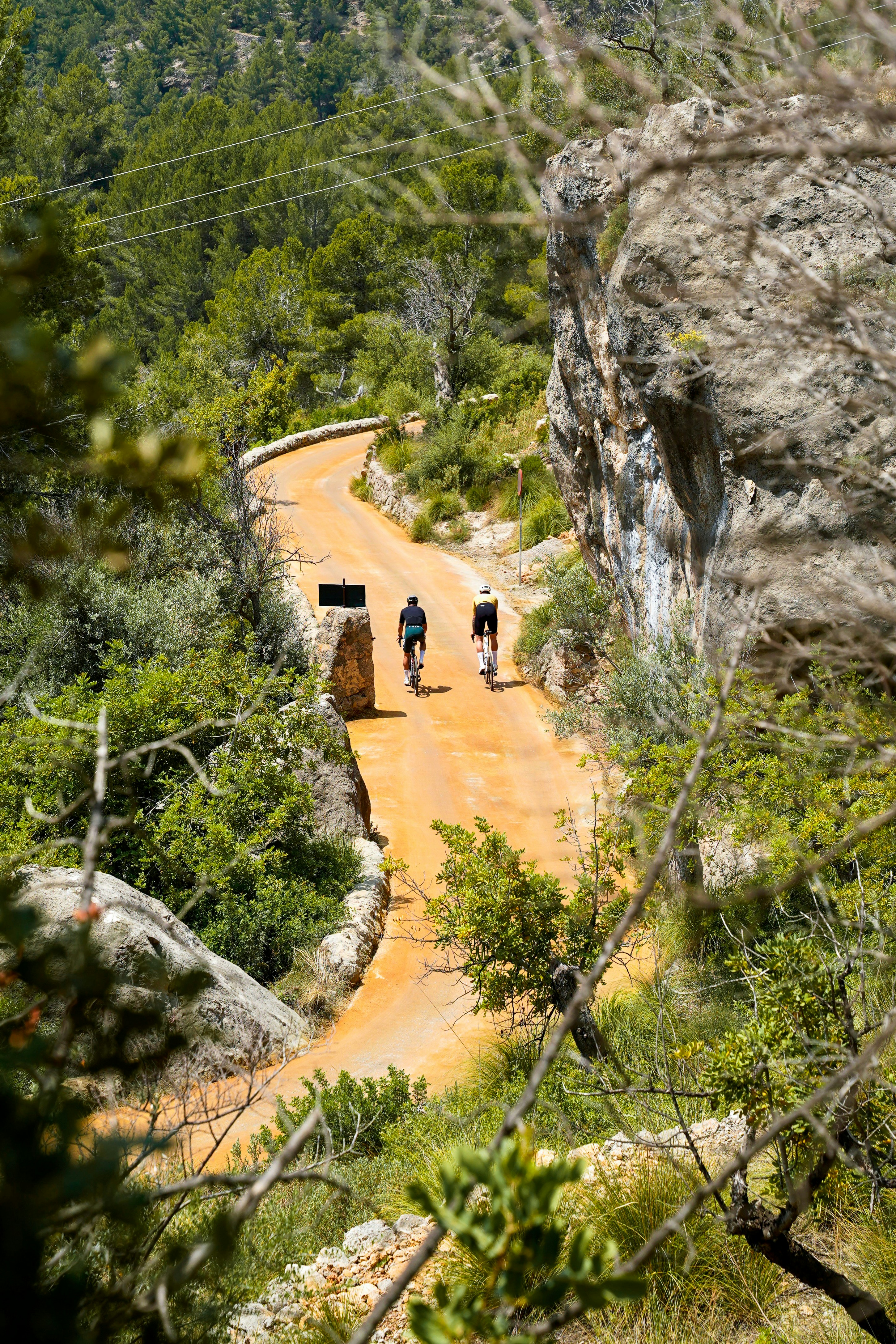 Two cyclists ride along a winding dirt road.