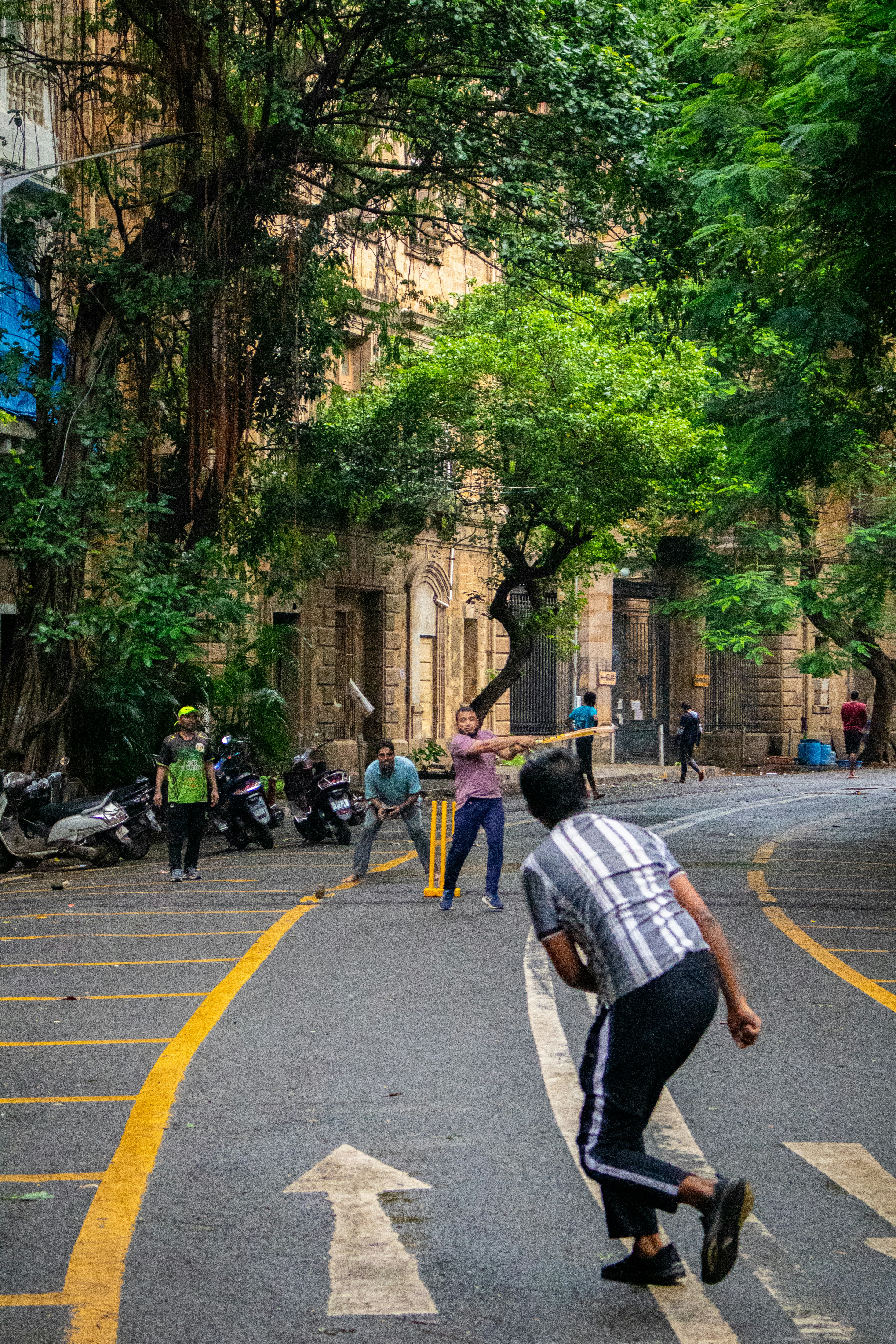 People play cricket in the middle of a street.