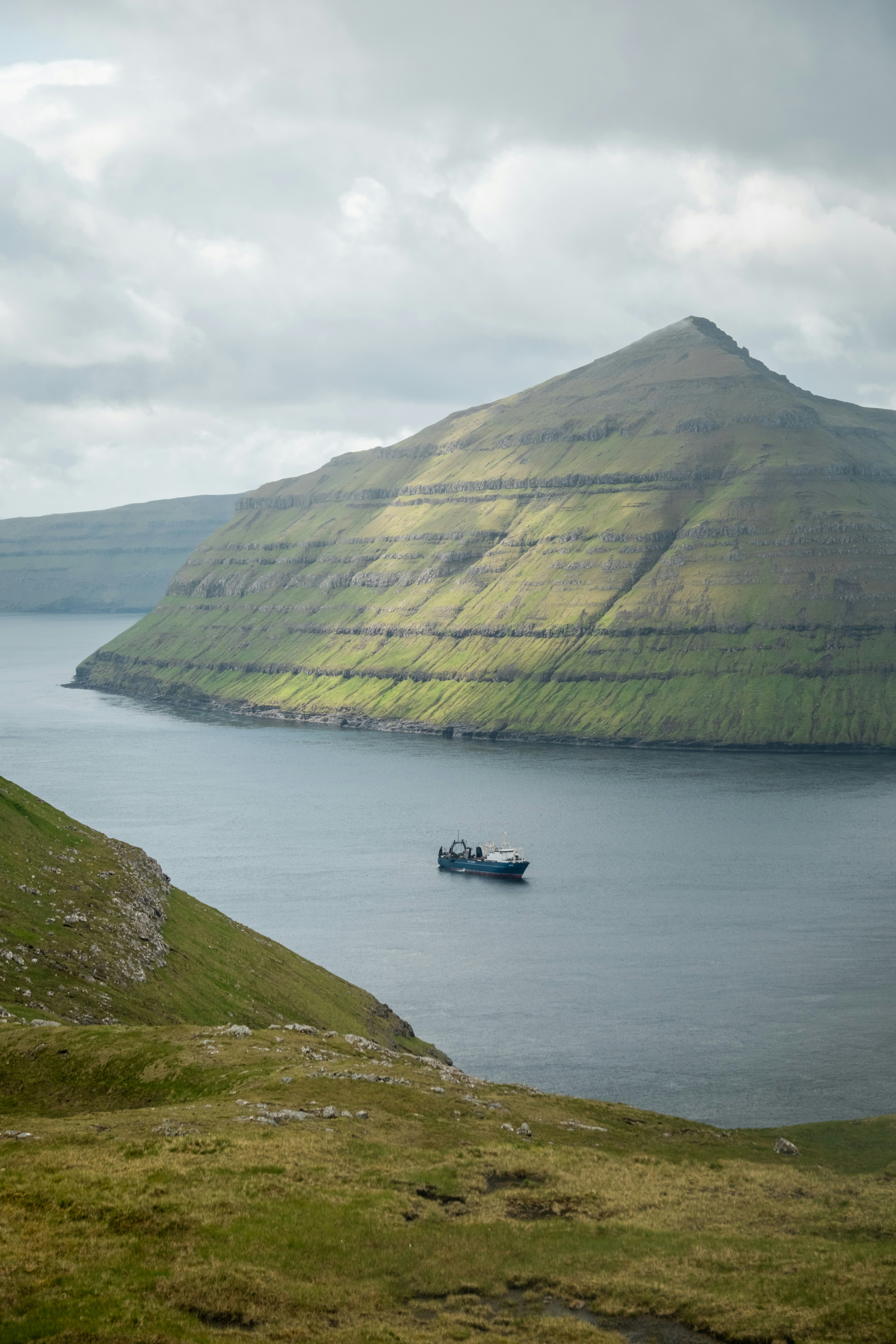 A boat sails in a bay by a mountain.