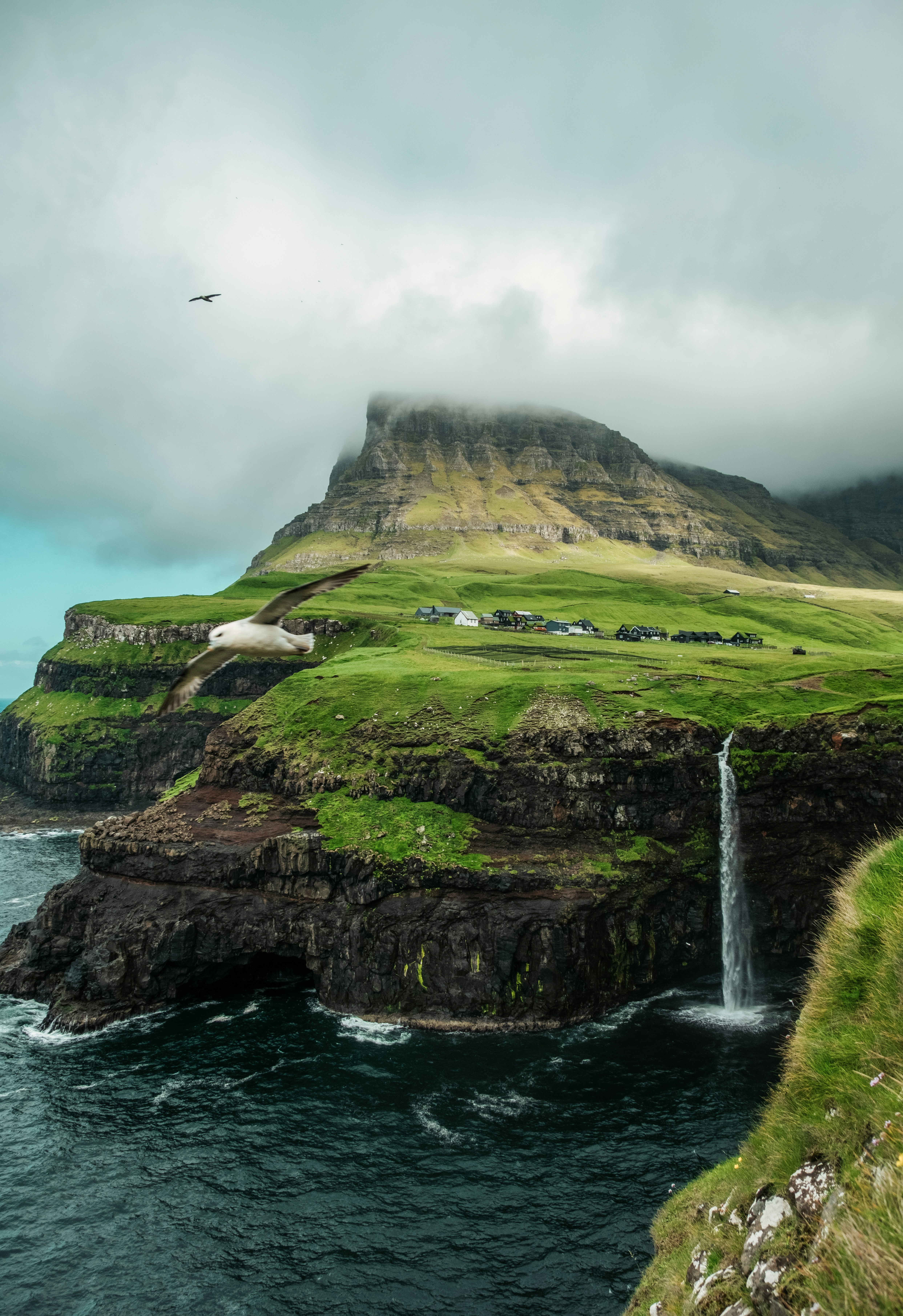 Dramatic waterfall and green hills meet the ocean.