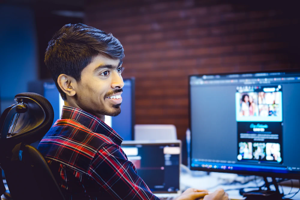 A student smiling at his desk, a computer screen beside him.