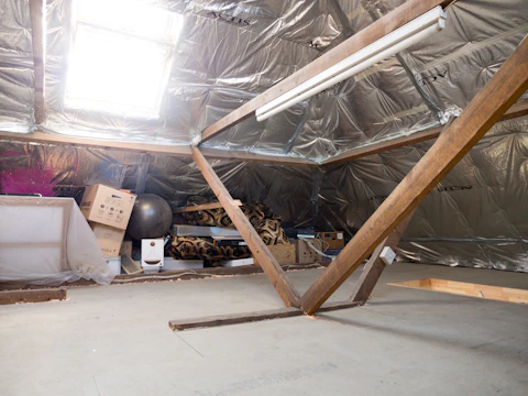 A dusty attic with insulation and wooden beams.