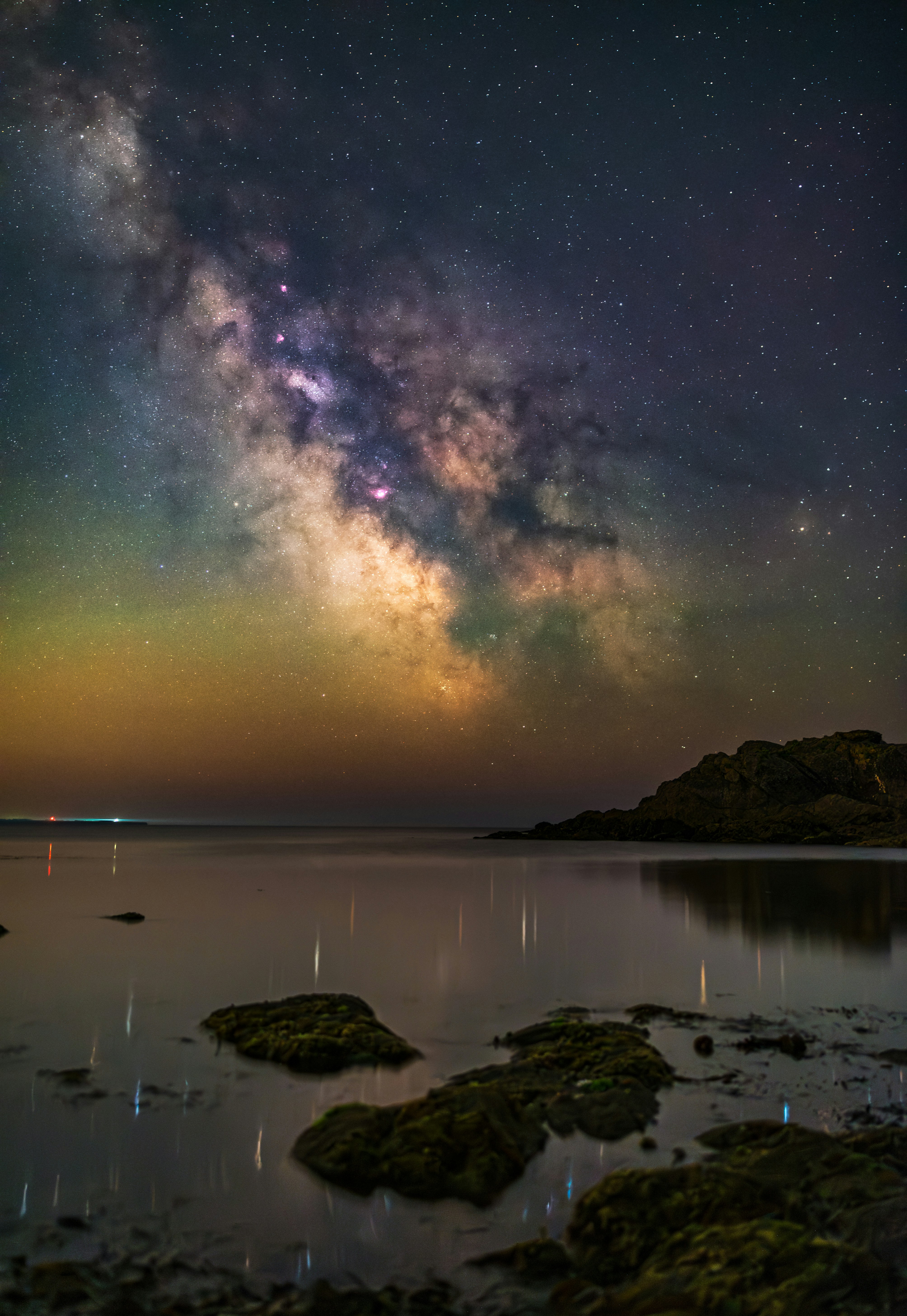 The milky way shines above the calm ocean.