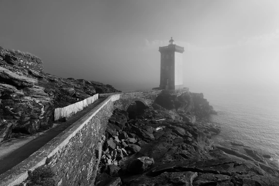 Lighthouse stands on the rocky coast in the fog.