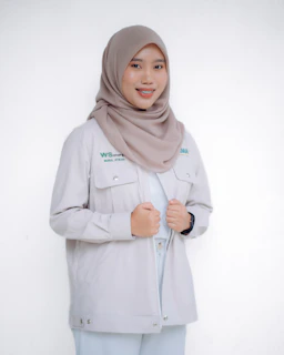 A smiling woman in a hijab and jacket is posing.