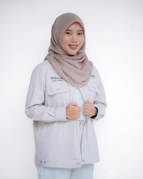 A smiling woman in a hijab and jacket is posing.