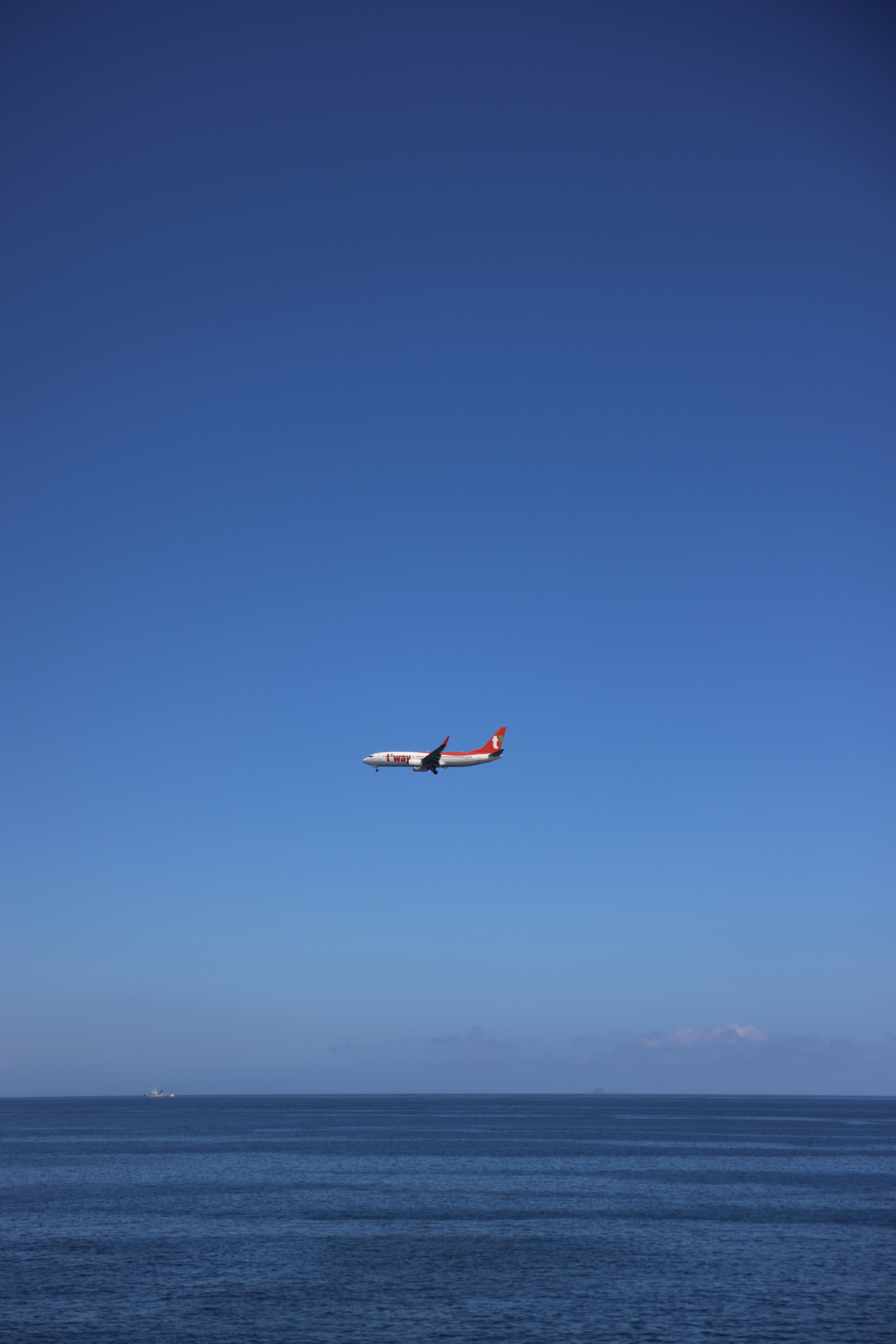 A plane flies over water under a blue sky.