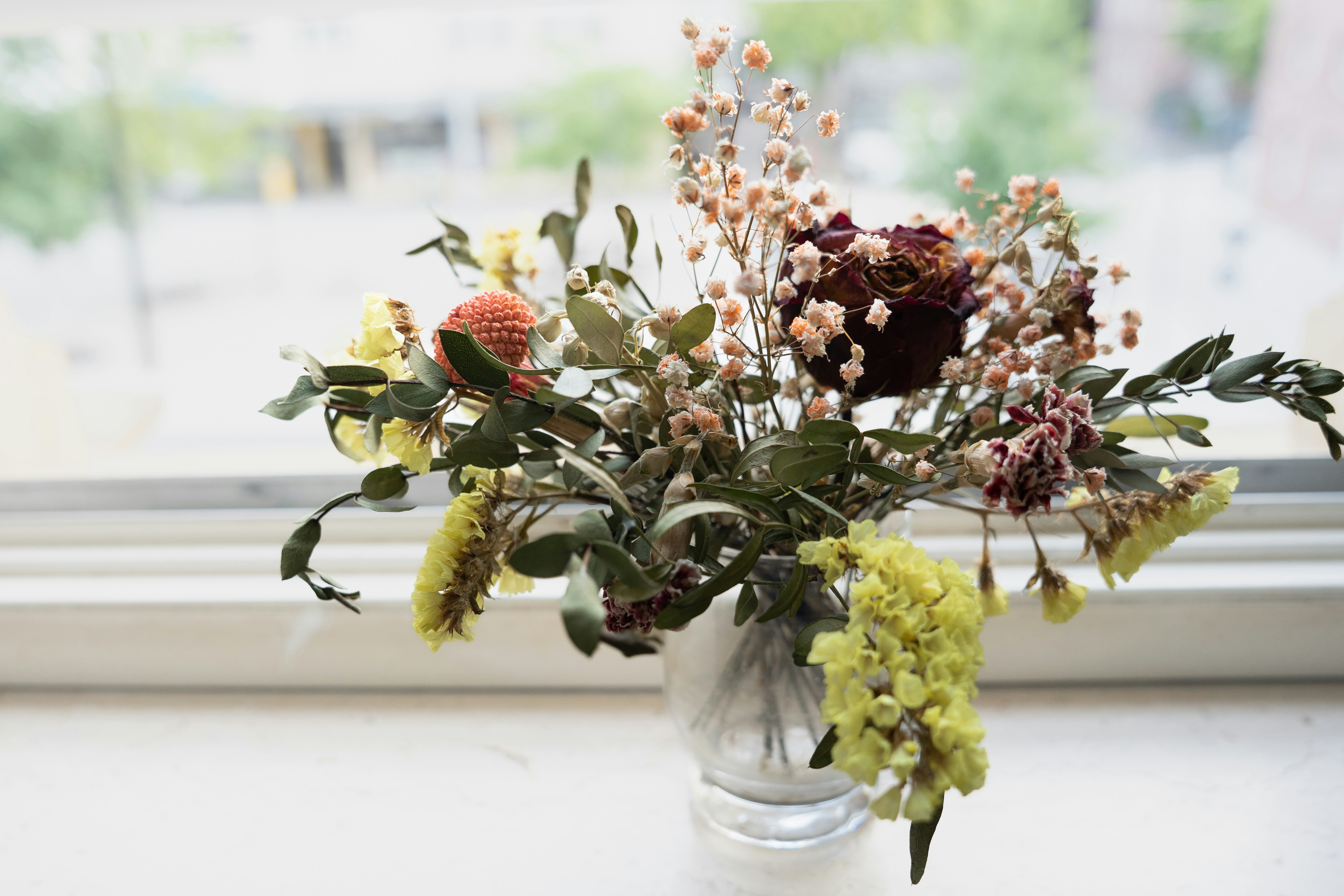 Dried flowers in a small vase sit by the window.